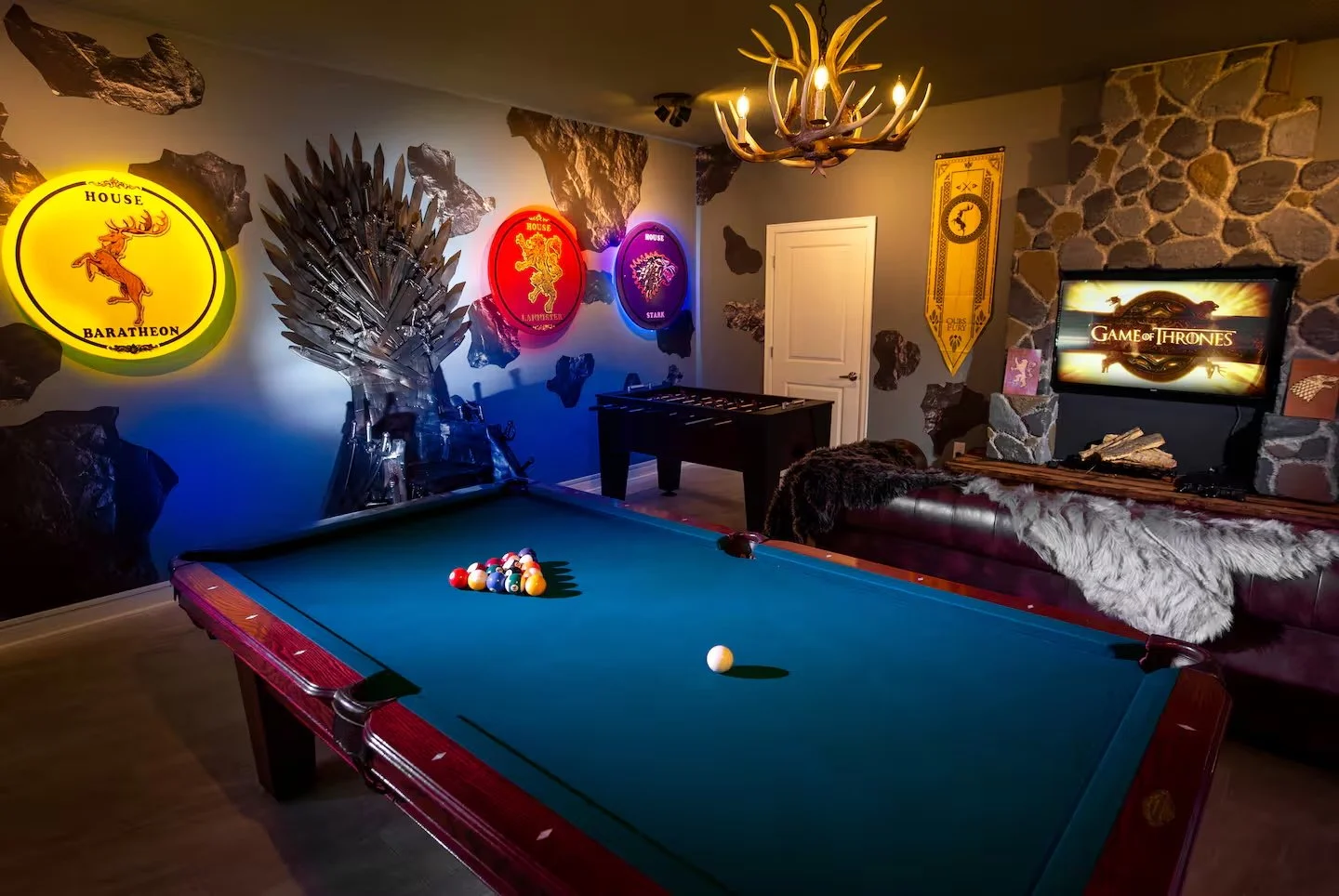 A game room featuring a pool table with billiard balls racked up, a TV displaying the 'Game of Thrones' logo, and illuminated house sigil signs on the wall. Game Room in vacation rental home in Storey Lake, Orlando Florida