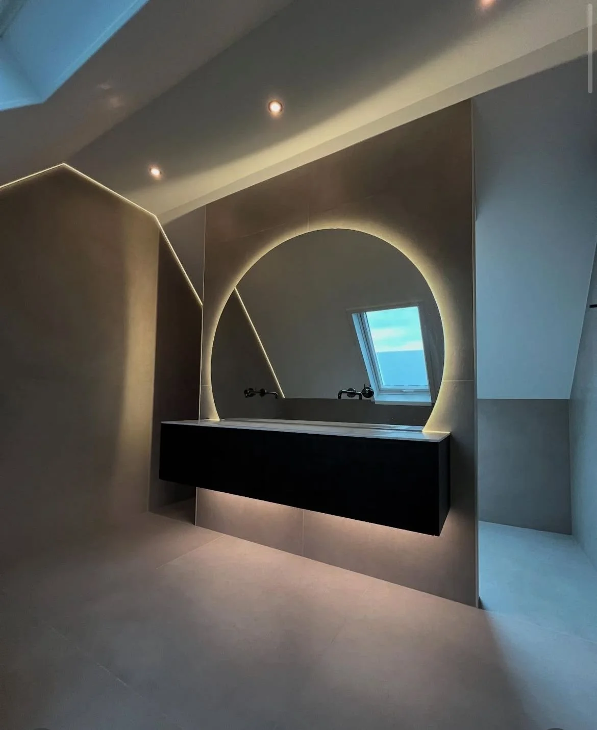 Witte vrijstaande badkuip in een moderne badkamer met marmeren tegels en een scheidingswand in beton, met een open trap en warm verlichting.