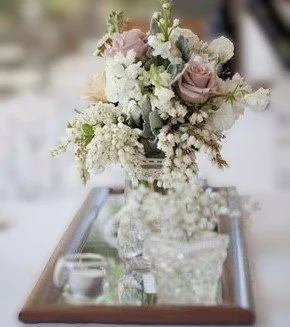 A floral centerpiece with pastel-colored roses and white flowers in a glass vase on a wooden table.
