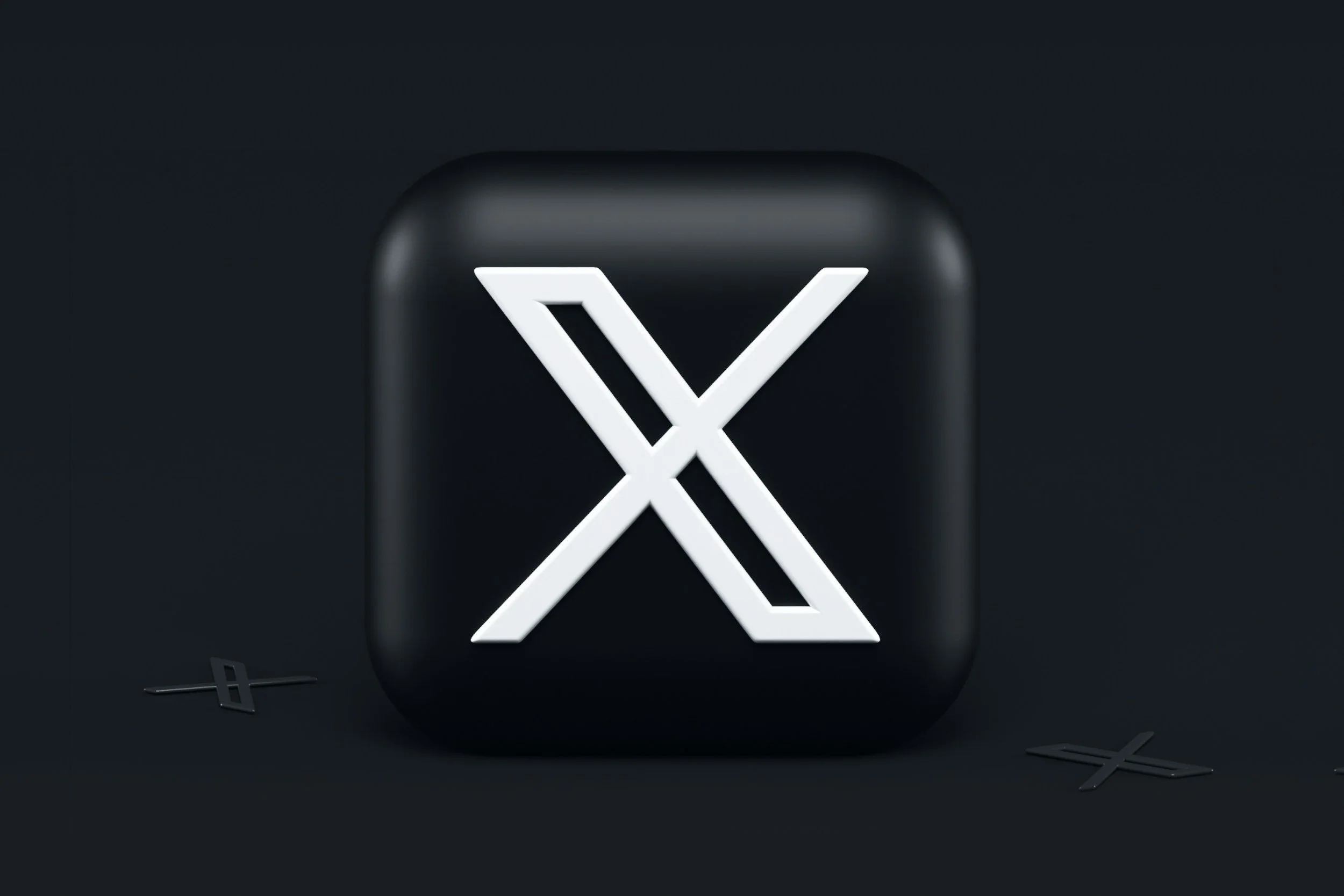 A black square with rounded edges displays a white stylized 'X' logo in the center, with several smaller black 'X' shapes scattered around it on a dark background.