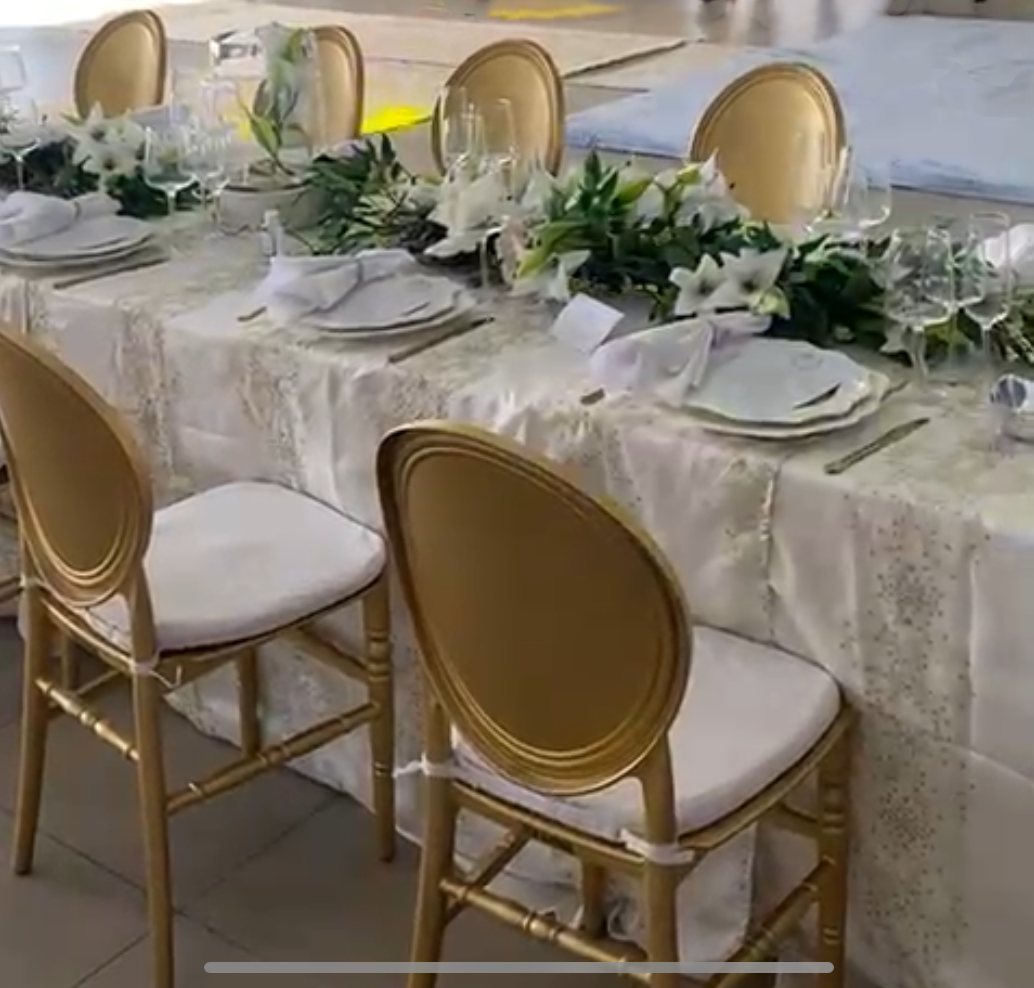 Elegant banquet table set for a formal event with gold chairs, white tablecloth, floral centerpiece, and place settings including plates, napkins, and glassware.