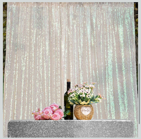 Decorative scene with a bottle of wine, pink roses, and a basket of white and pink flowers on a glittery surface backdrop with shimmering curtain.