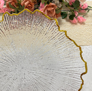Decorative glass plate with gold edge, placed on a surface with pink and brown flowers in the background.