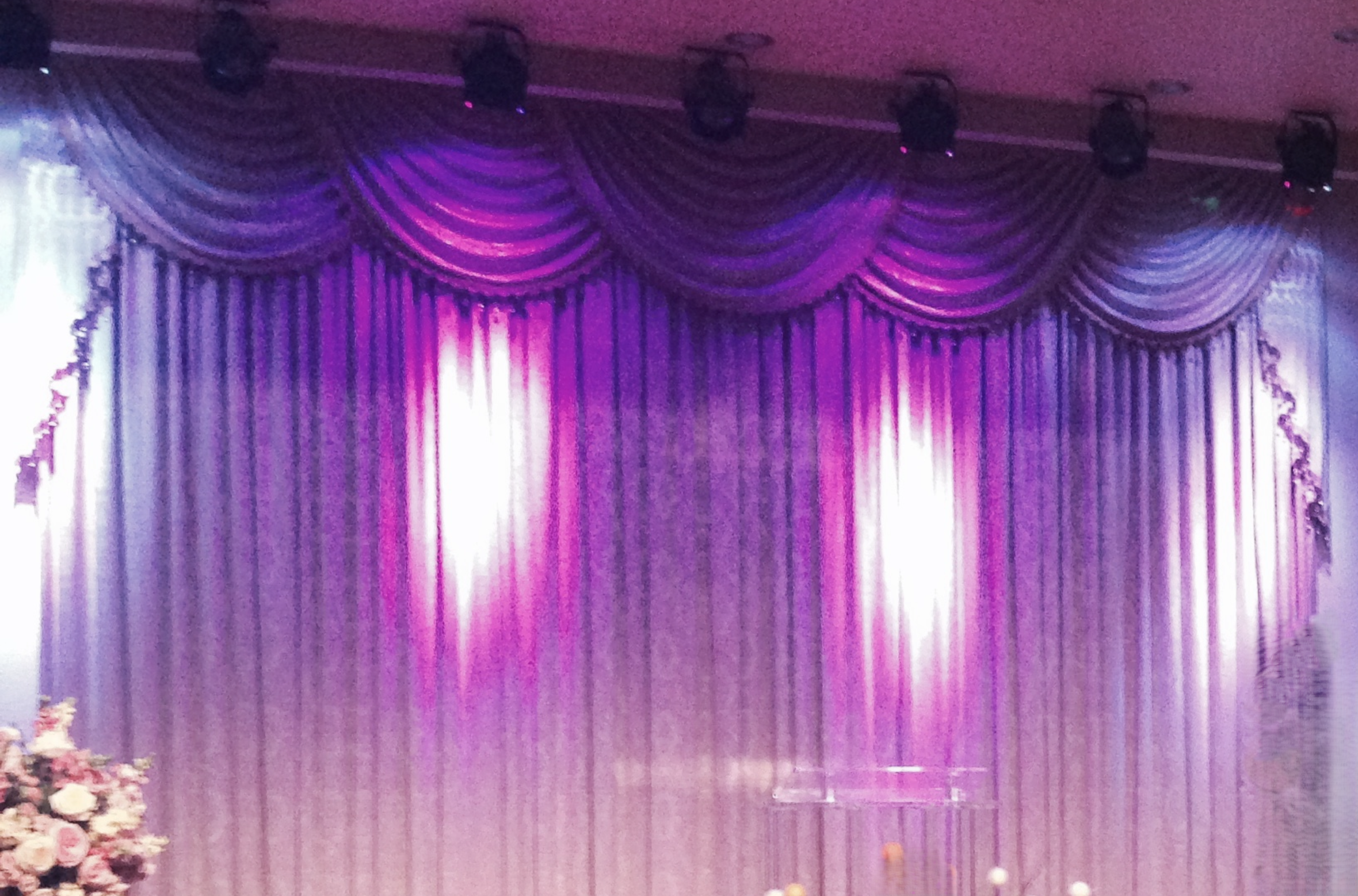 Curtains in purple, lavender, and gold shades with swag valances and tiebacks, set up on a stage with lighting.