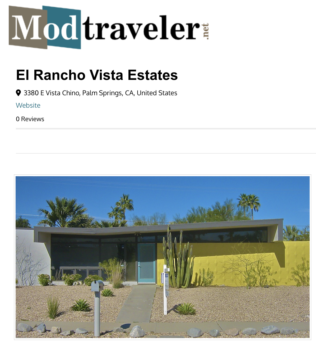 A modern, single-story house with a flat roof, blue front door, and distinctive bright yellow wall. The front yard features desert landscaping with rocks, small bushes, and a large cactus. Palm trees and a clear blue sky are visible in the background.