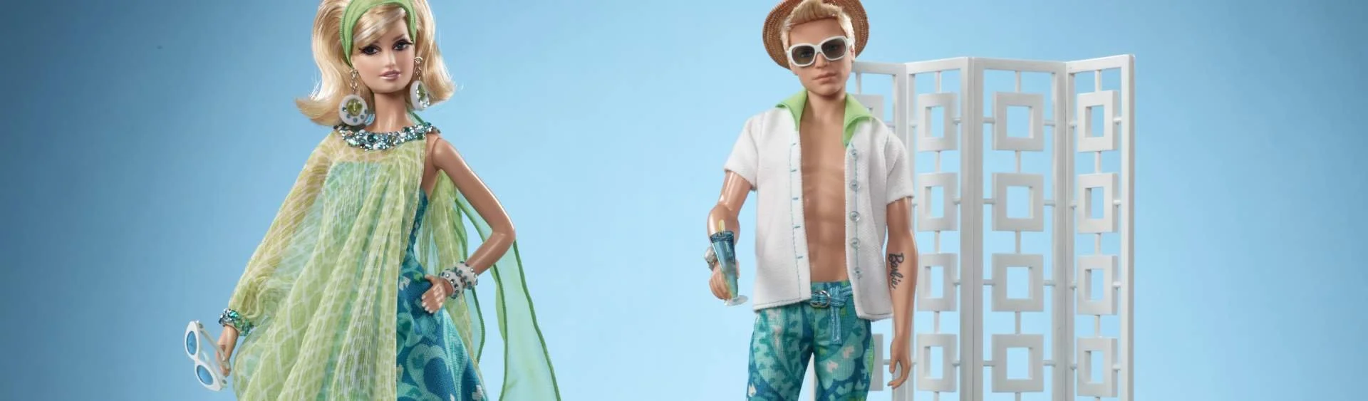 Barbie doll and a male doll dressed in summer clothing standing in front of a pale blue backdrop.