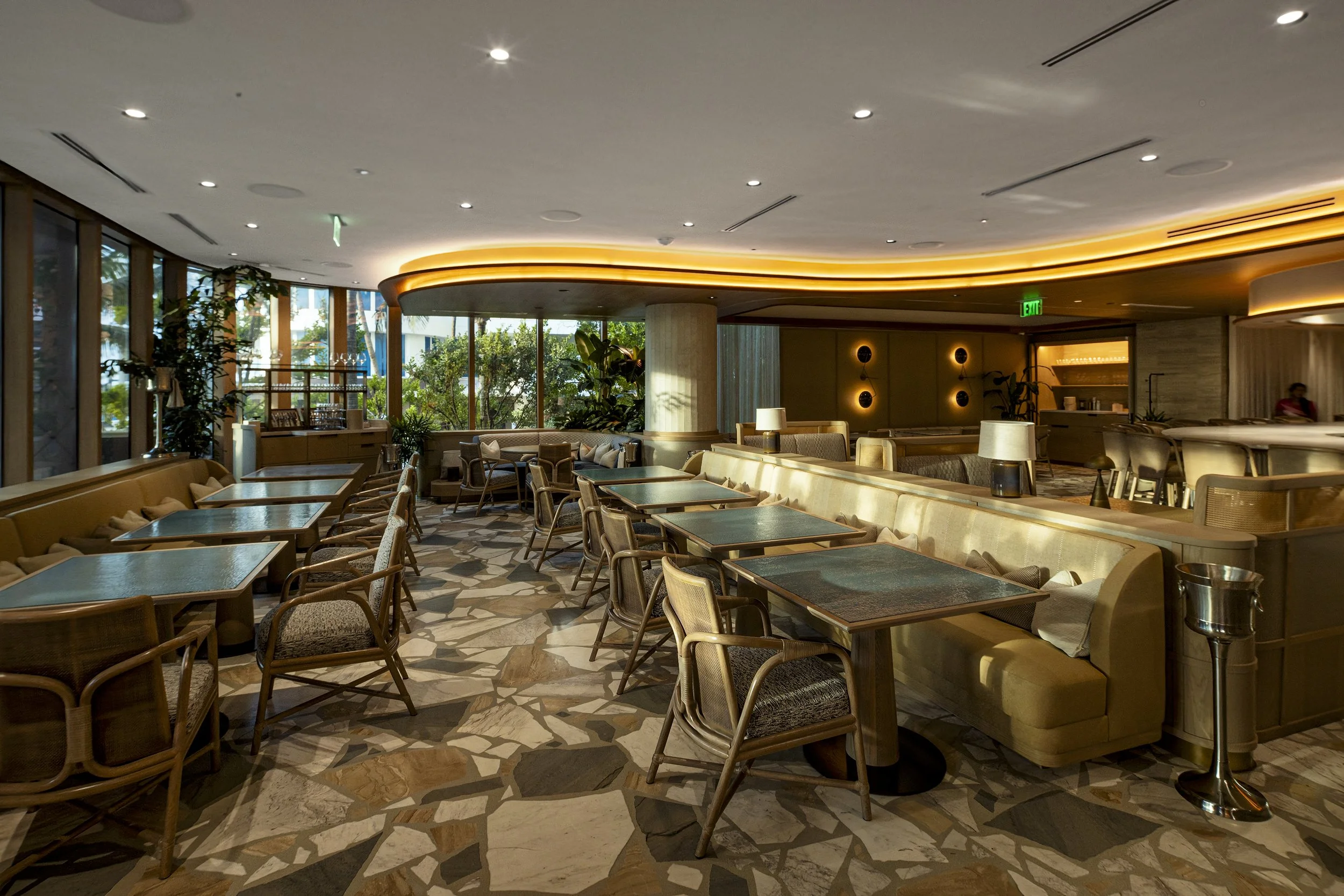 Modern upscale restaurant interior with tables, chairs, and large windows showing greenery outside.