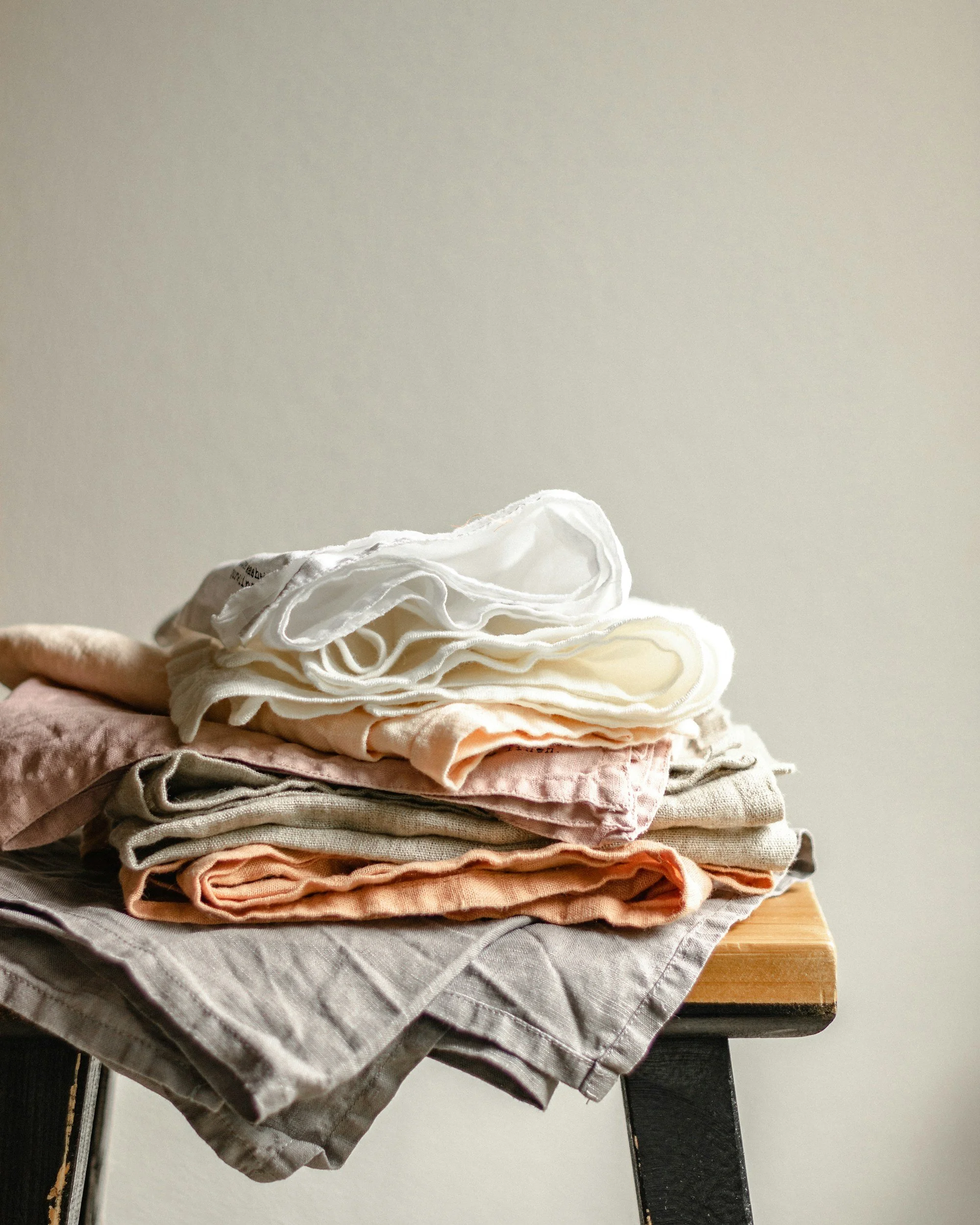 Stack of folded clothes on a wooden table against a plain wall.