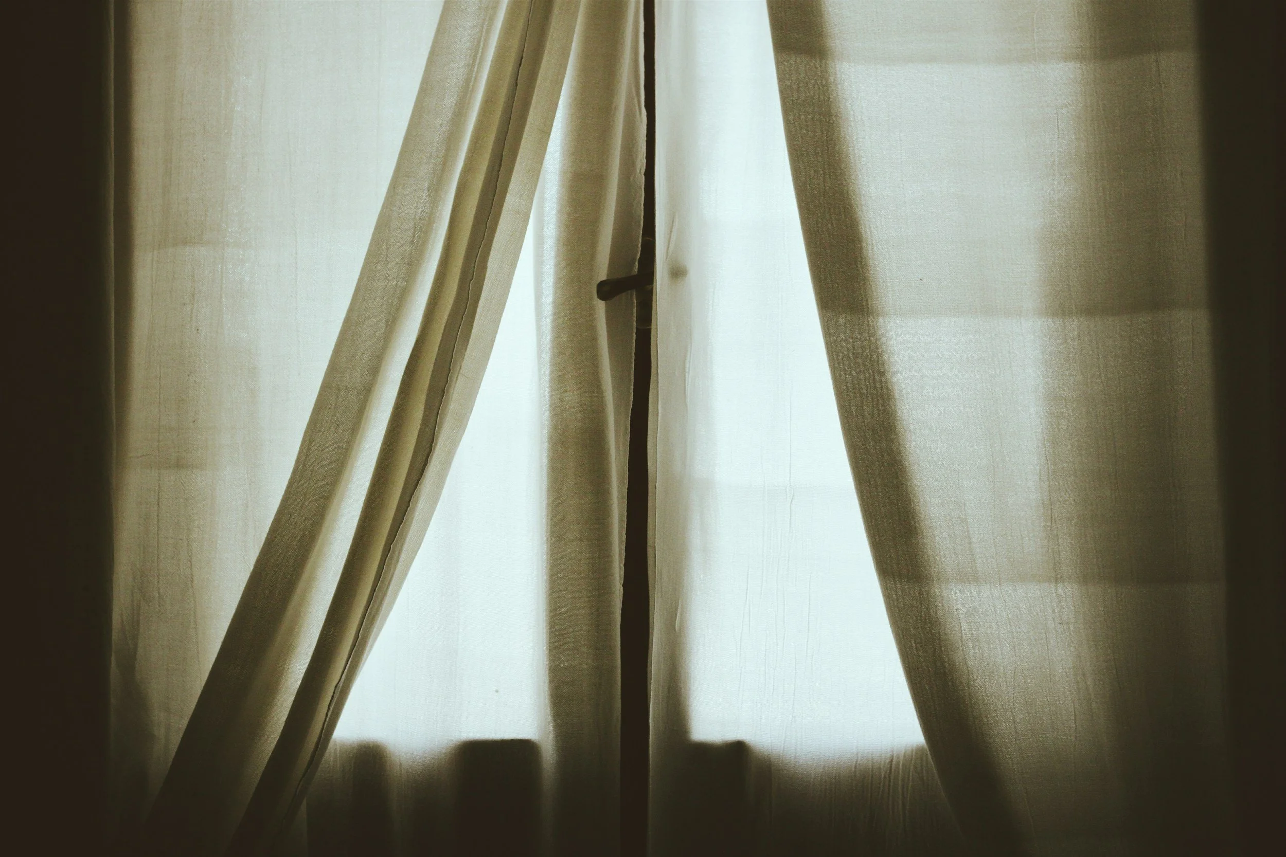 Closed beige curtains with light shining through in the background.