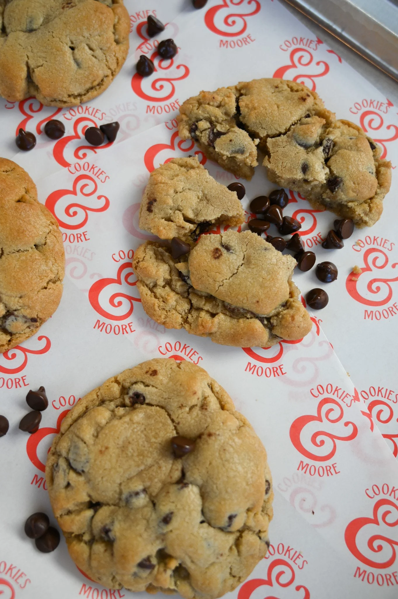 Chocolate chip cookies on branded parchment paper with cookie crumbs and scattered chocolate chips.