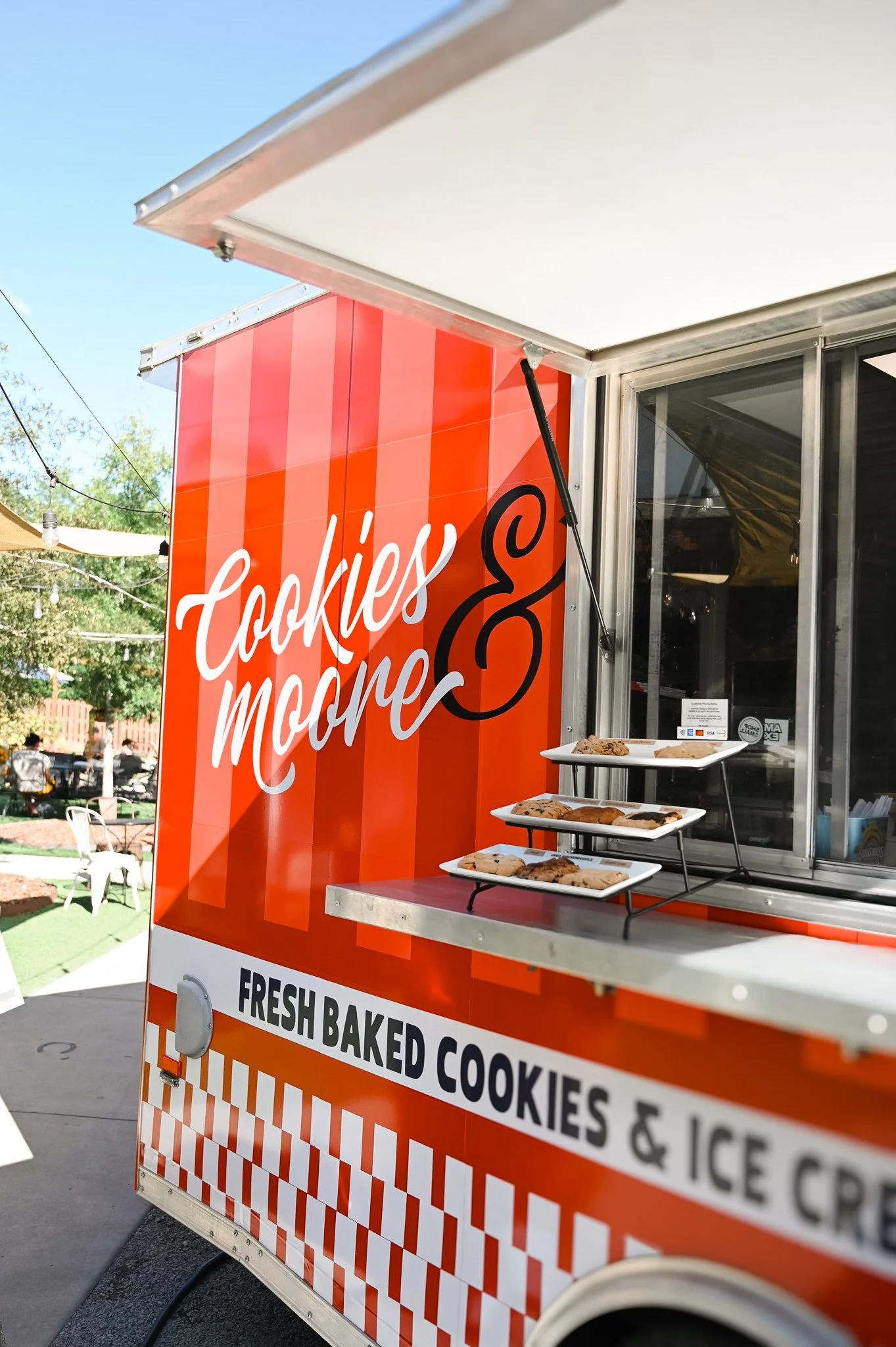 Cookies & Moore Food Truck parked at Red's Corner, in Southern Pines NC with a smaller sign below advertising 'Fresh baked cookies & ice cream.' There are three white trays with cookies on a small shelf outside the window.