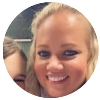 Close-up of a smiling blonde woman with blue eyes, partially obscured by another person, against a slightly blurred background.