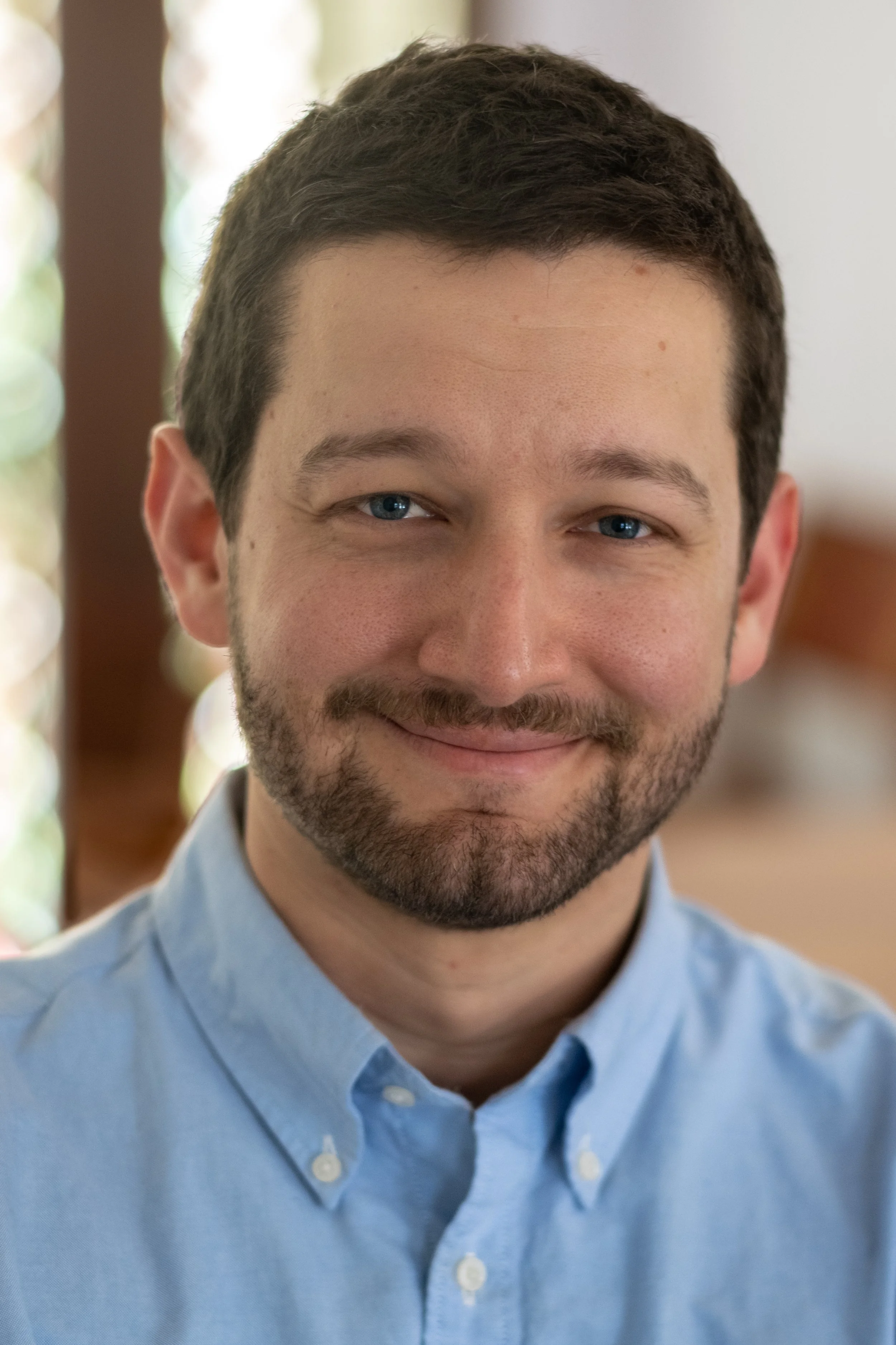 Close-up of dan gutterman. He has short dark brown hair, blue eyes, and a beard, smiling and wearing a light blue button-up shirt.