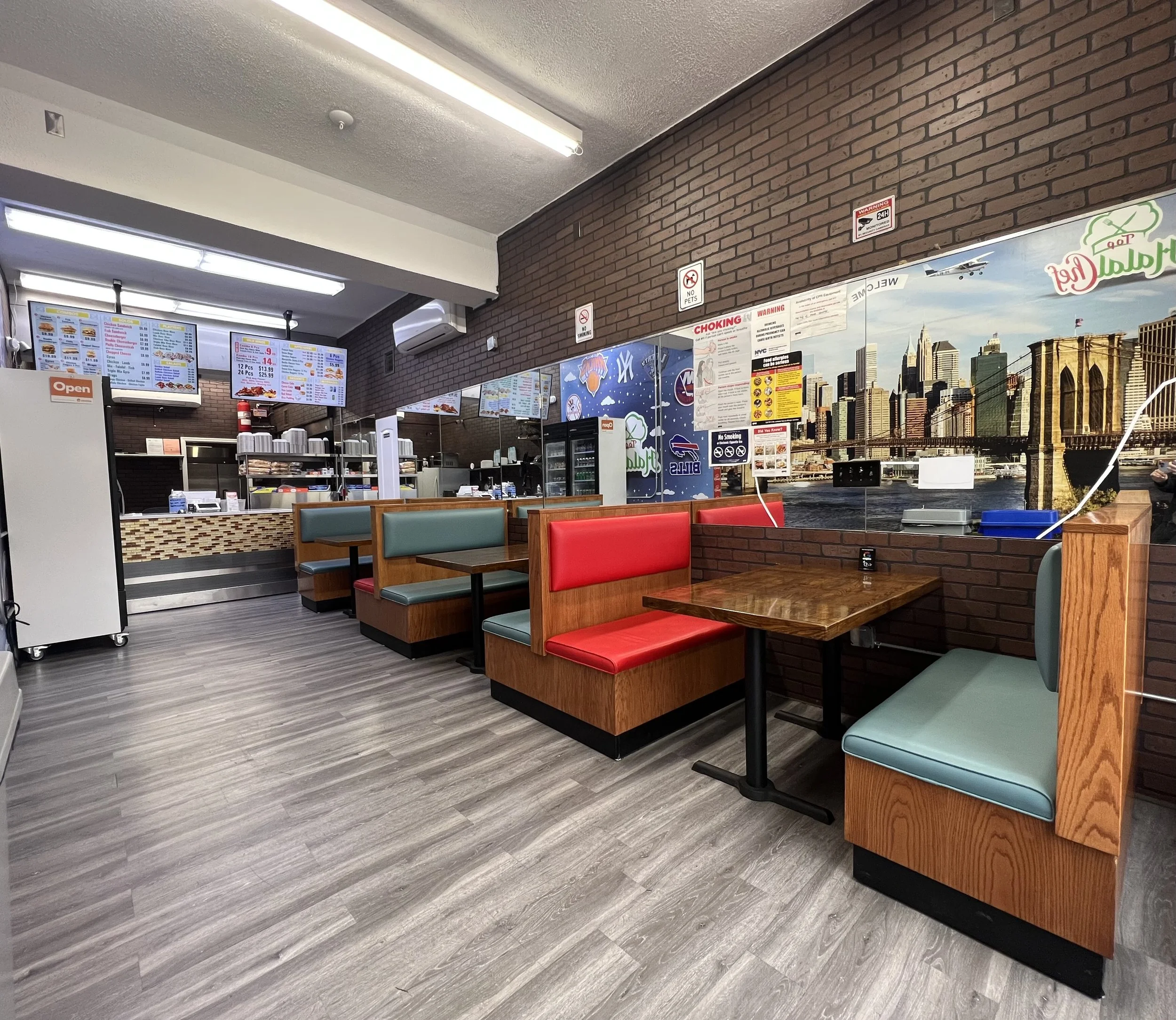 Inside a fast food restaurant with booth seating, brick walls, and a view of the New York City skyline and Brooklyn Bridge mural.