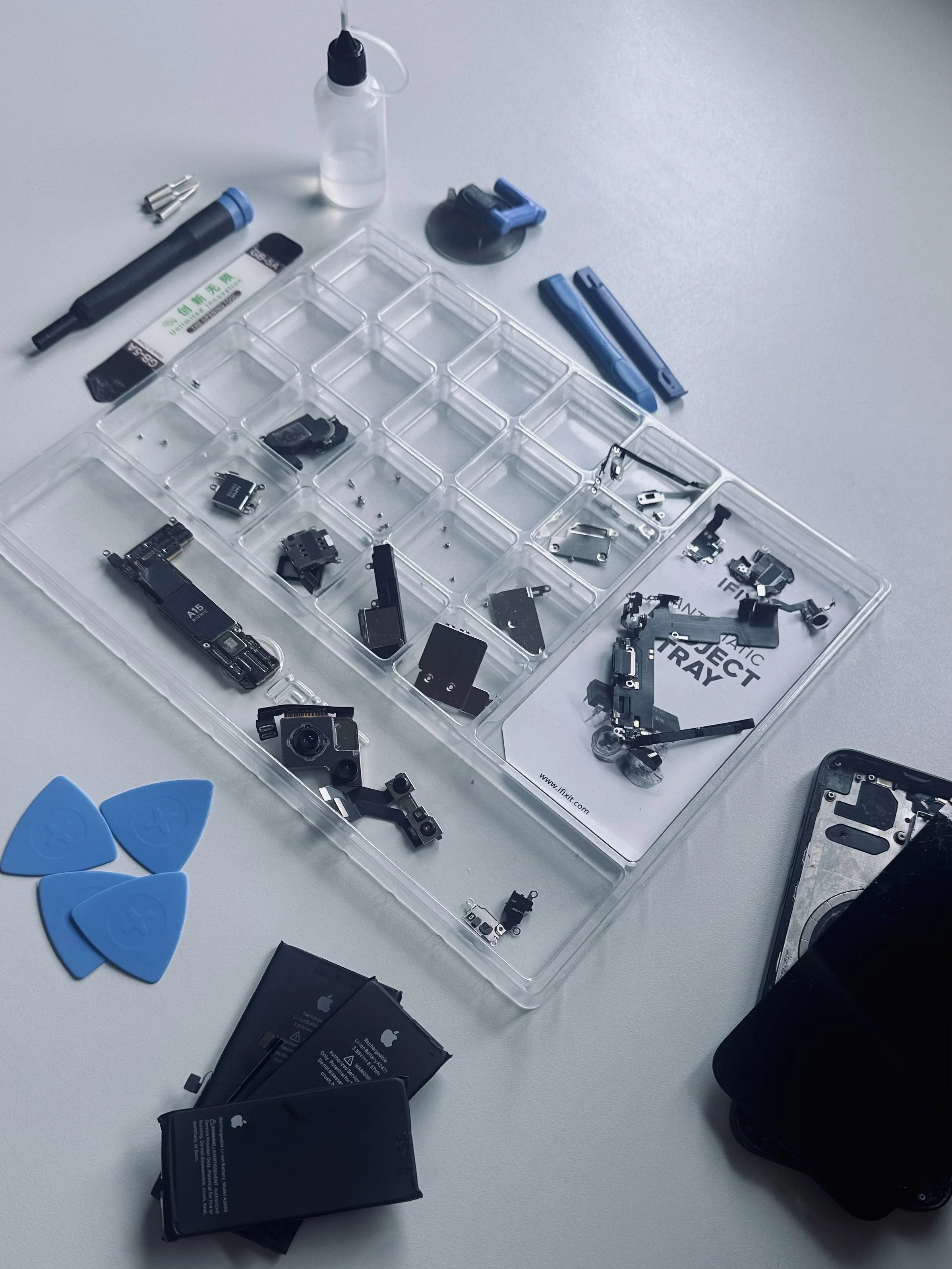 Auf dem Tisch sind verschiedene Handyreparaturteile, Werkzeuge und Ersatzteile, darunter Batterien, Kondensatoren, Mikrofone, Schrauben und Plastikteile, die für die Reparatur eines Smartphones verwendet werden.