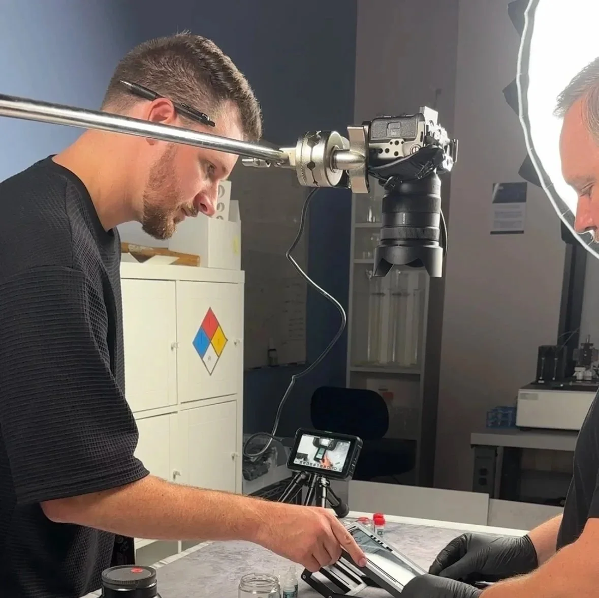Two scientists working in a laboratory with specialized equipment, one of whom is pointing at an object on the table, while the other observes.