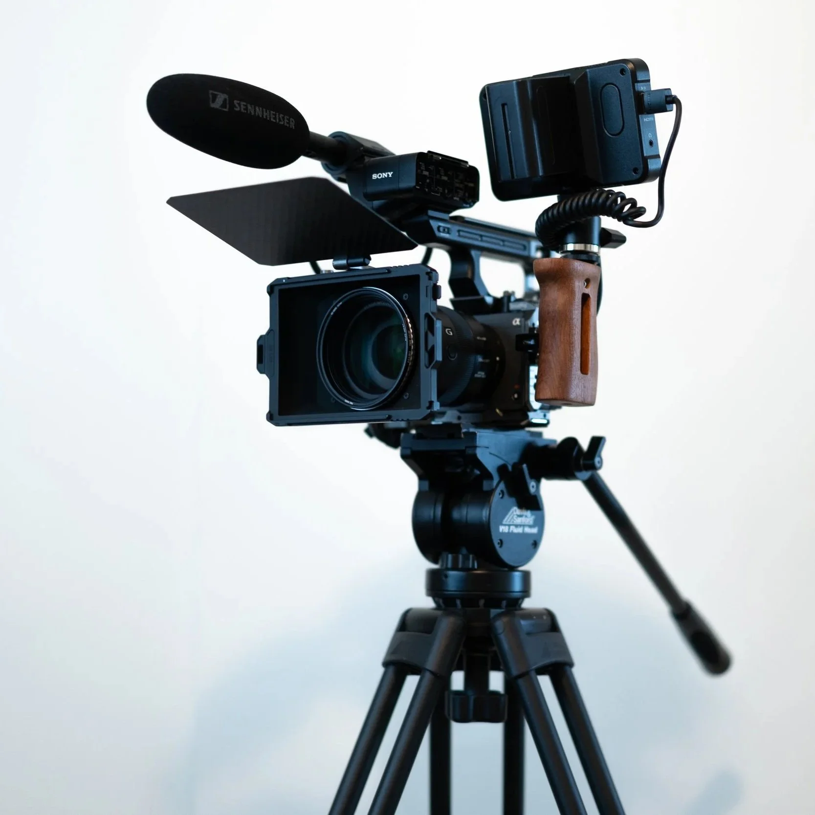 Professional camera mounted on a tripod with a microphone and various accessories.