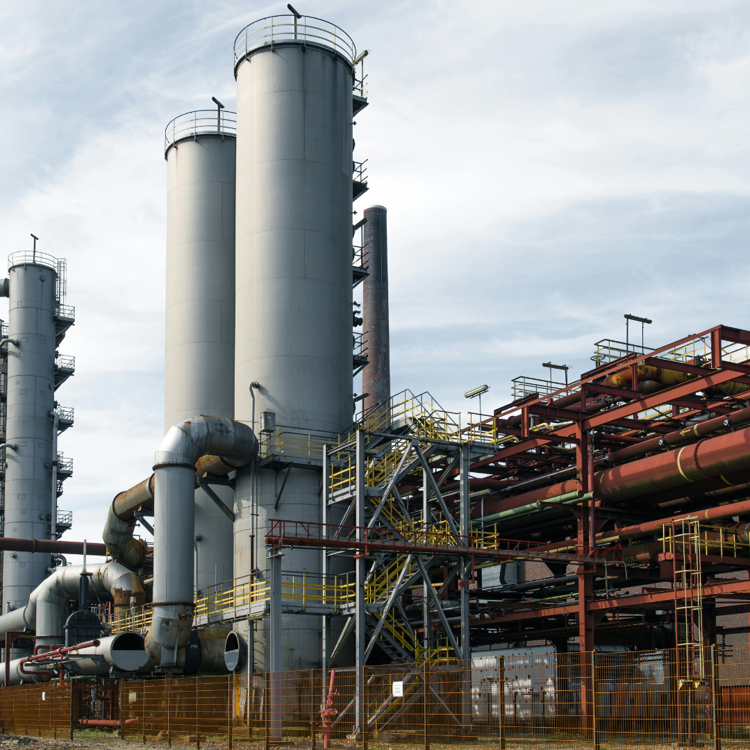 Industrial refinery with large cooling towers, pipes, and metal structures under a cloudy sky.