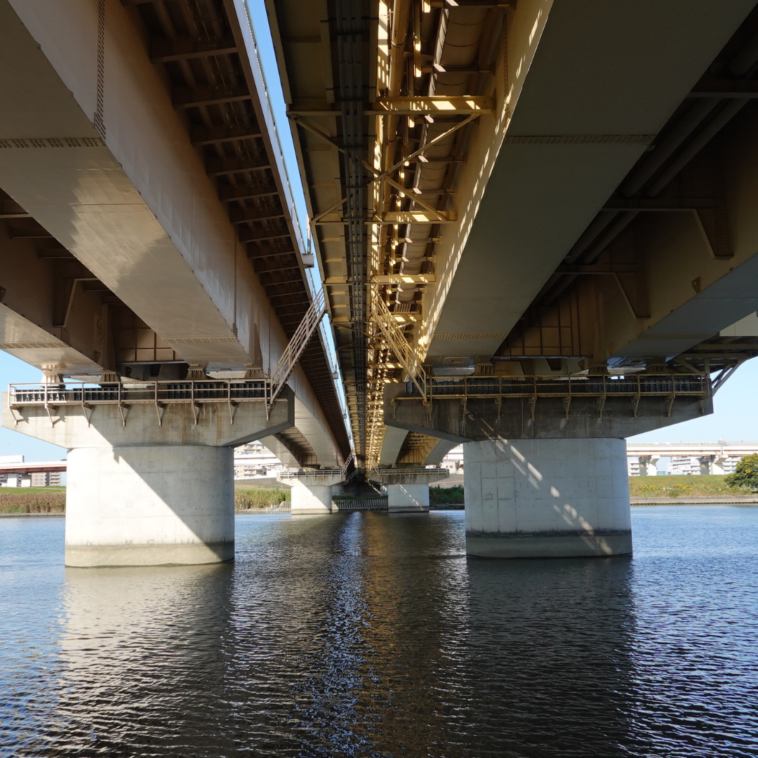 Underneath a large bridge over water, showing the underside, supports, and structure of the bridge.