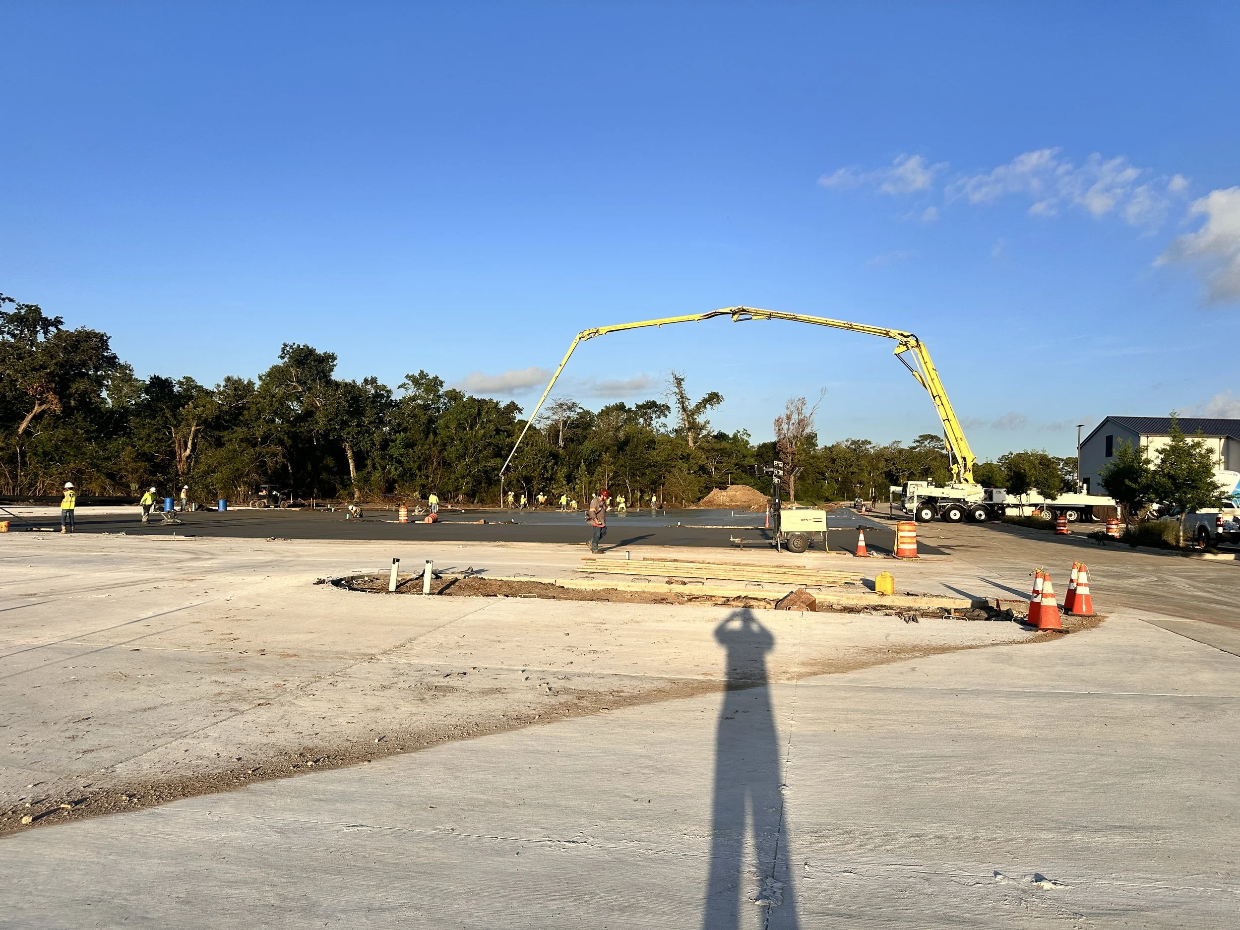 Construction site with workers, orange cones, and a concrete pouring truck under a clear blue sky.