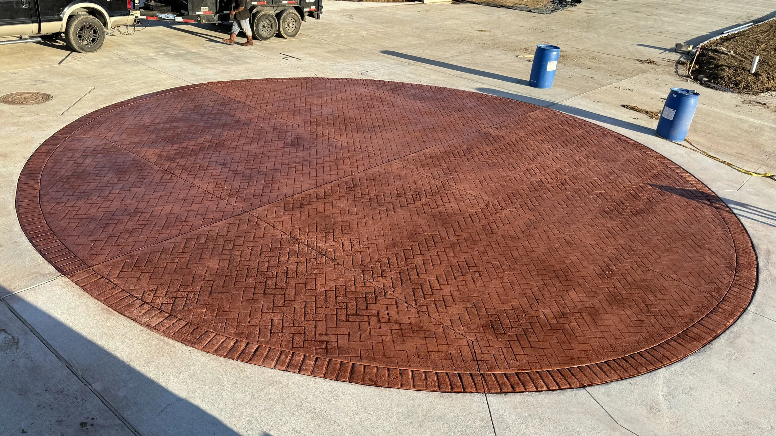 A circular area with red brick paving stones, surrounded by a concrete surface, with construction equipment and tools nearby.