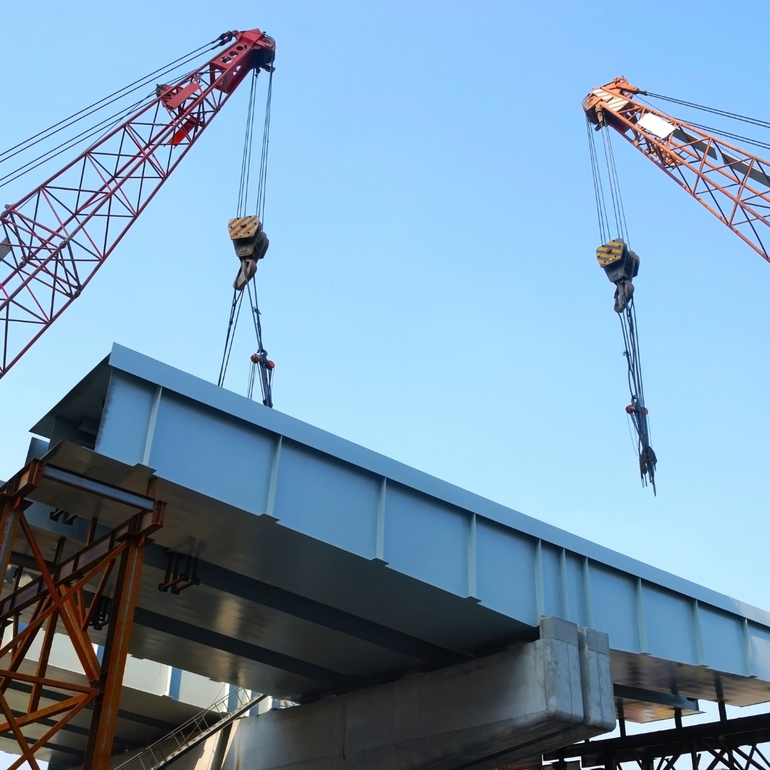 Two construction cranes are lifting a large steel beam into place during a building construction project.
