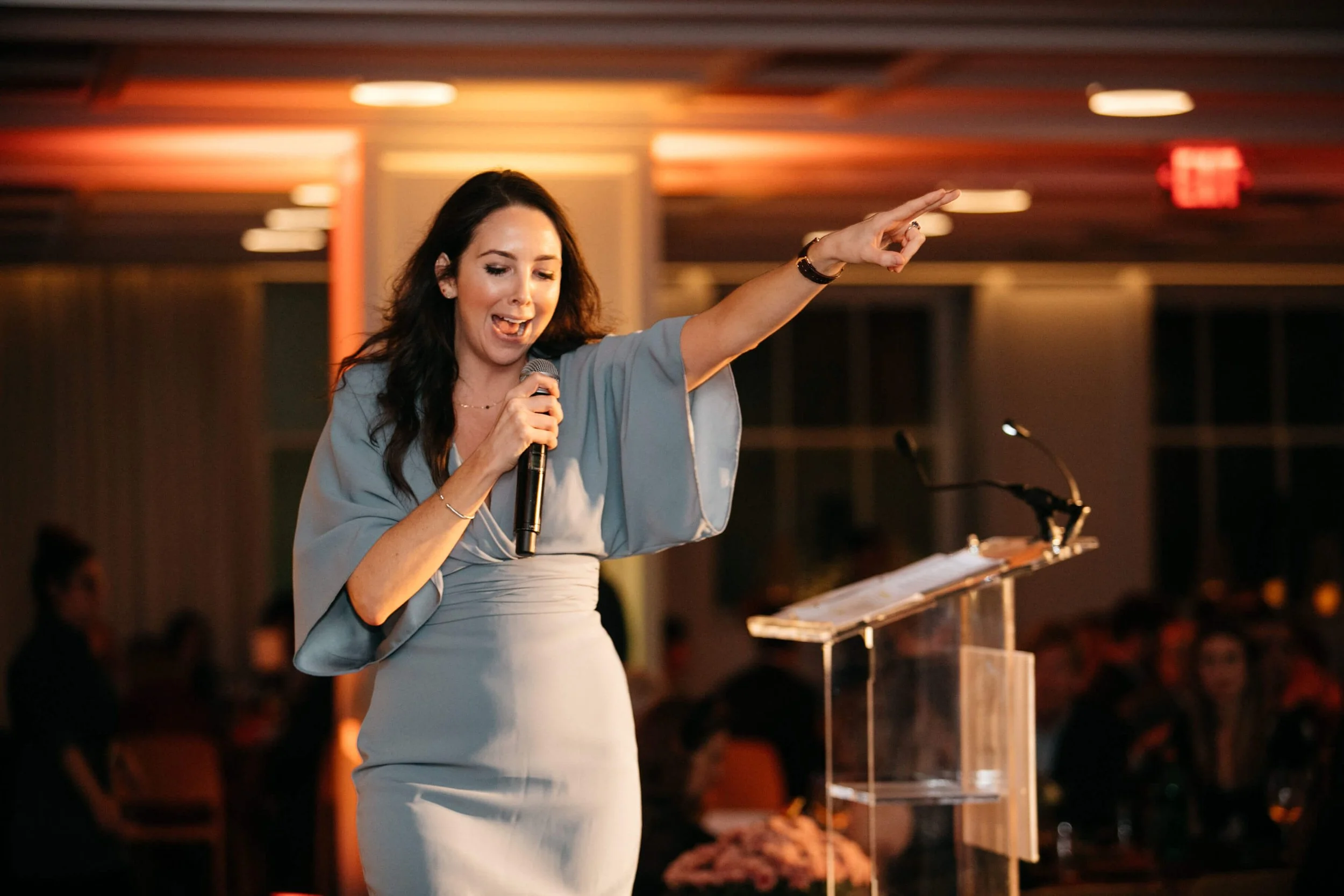 Jacqueline Towers-Perkins in a blue dress speaking into a microphone at a podium during an indoor event.