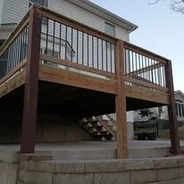 Wooden deck with metal railing and stairs leading down to the ground level, attached to a residential house.