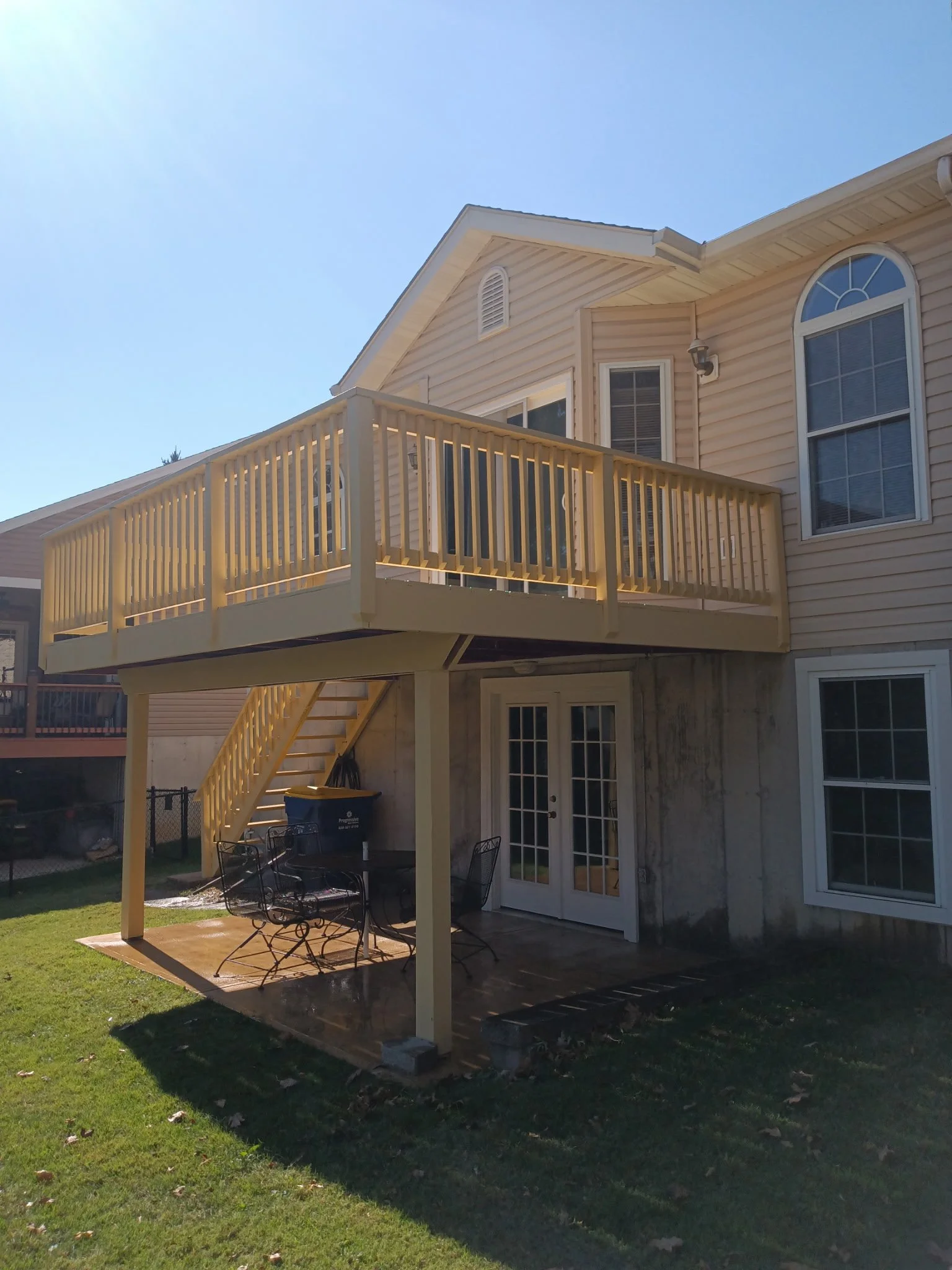 Backyard with a wooden deck and railing, outdoor table and chairs, French doors, and a beige house with multiple windows and a second-story balcony.