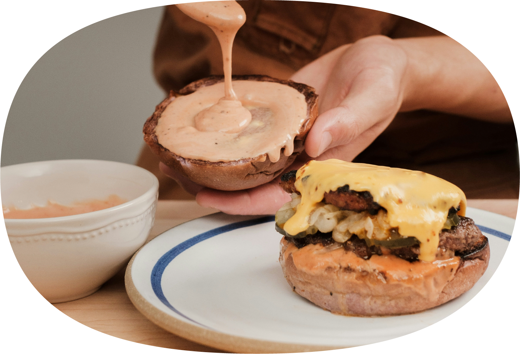 Pessoa colocando molho em hambúrguer com queijo, carne e alface em um prato