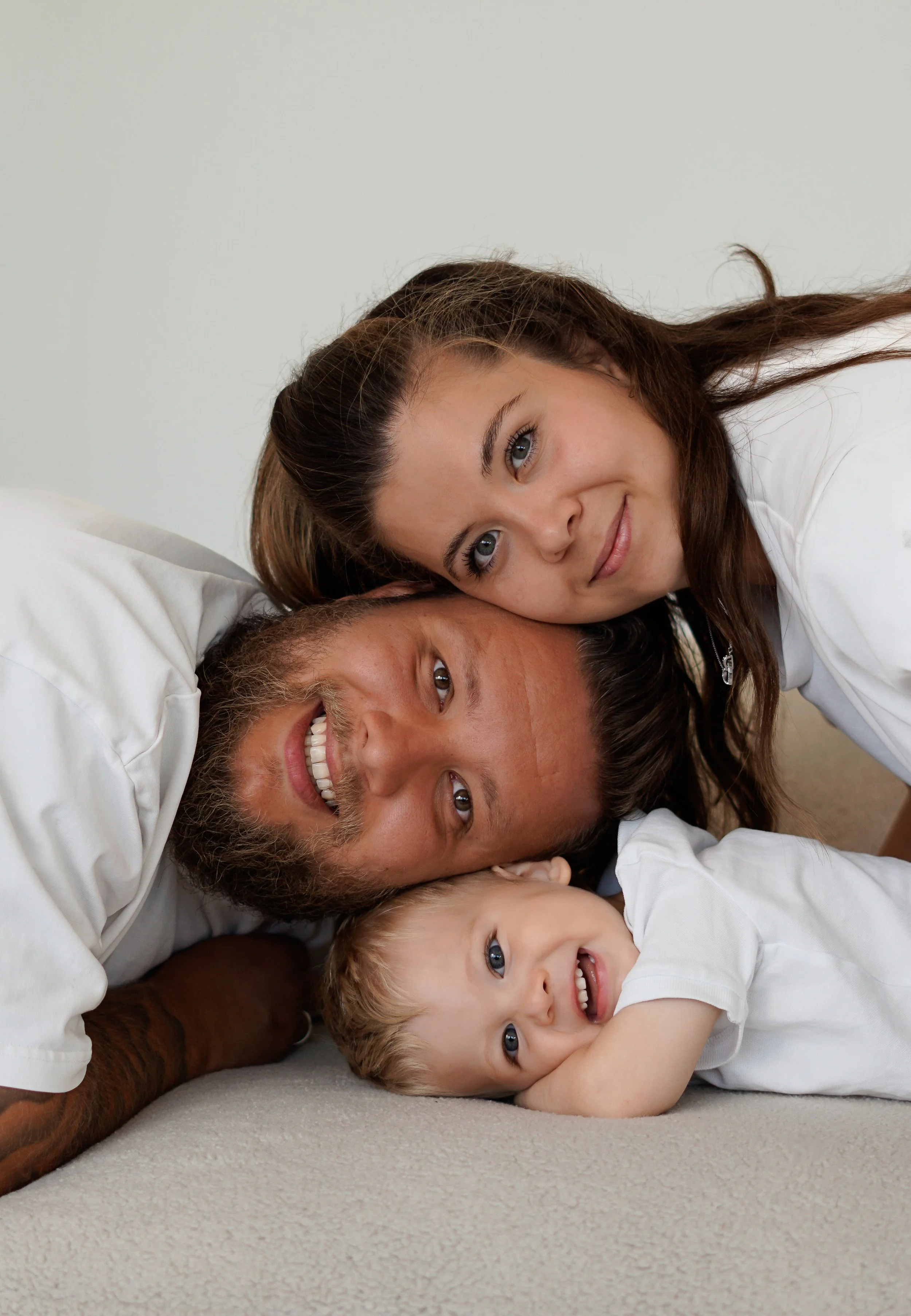 A happy family of three laying on a bed, with a woman, man, and young boy cuddling together.