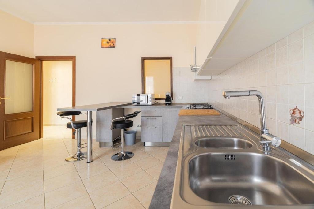 Cucina con doppio lavandino, piano di lavoro in pietra, stufa a gas, armadietti e pareti rivestite di piastrelle beige