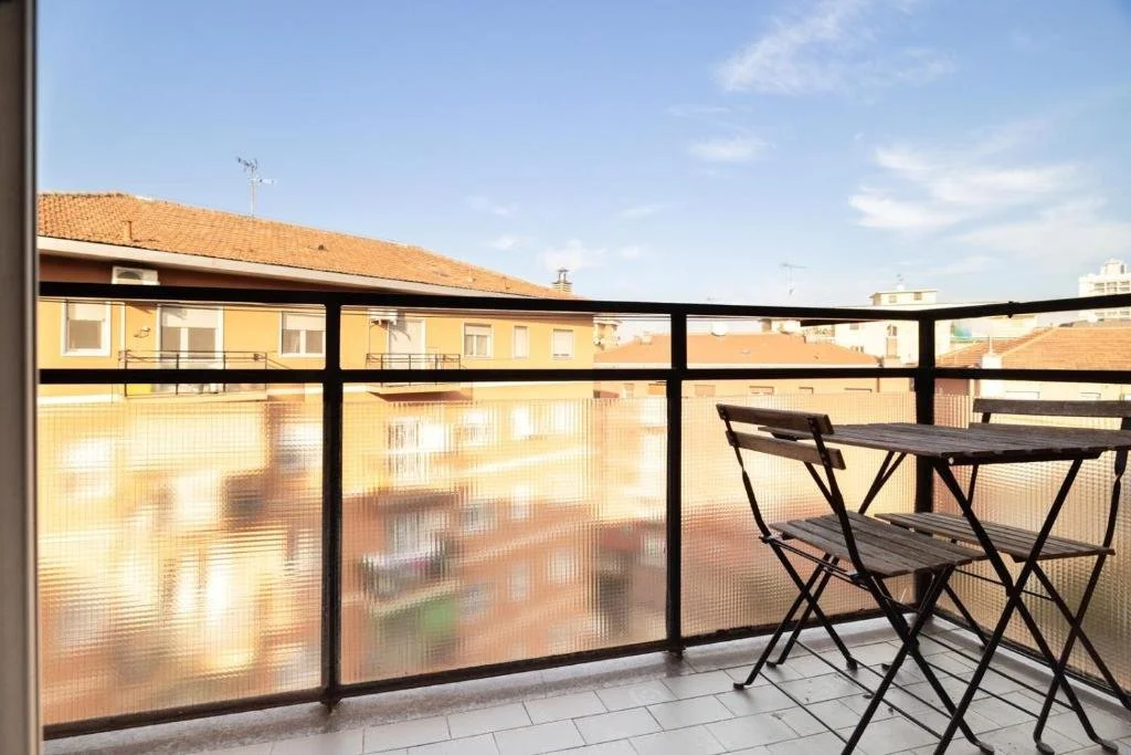 Balcone con tavolo e sedie in legno, vista su edifici residenziali con tetti rossi e un cielo sereno.