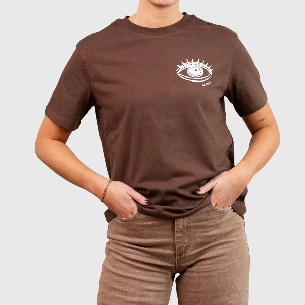 Kvinna i brun oversize t-shirt med ögonlogga på bröstet