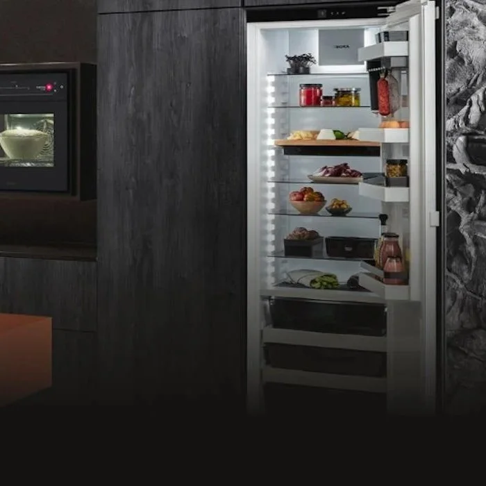 Open refrigerator filled with various food items including fruits, vegetables, and condiments, in a modern kitchen.