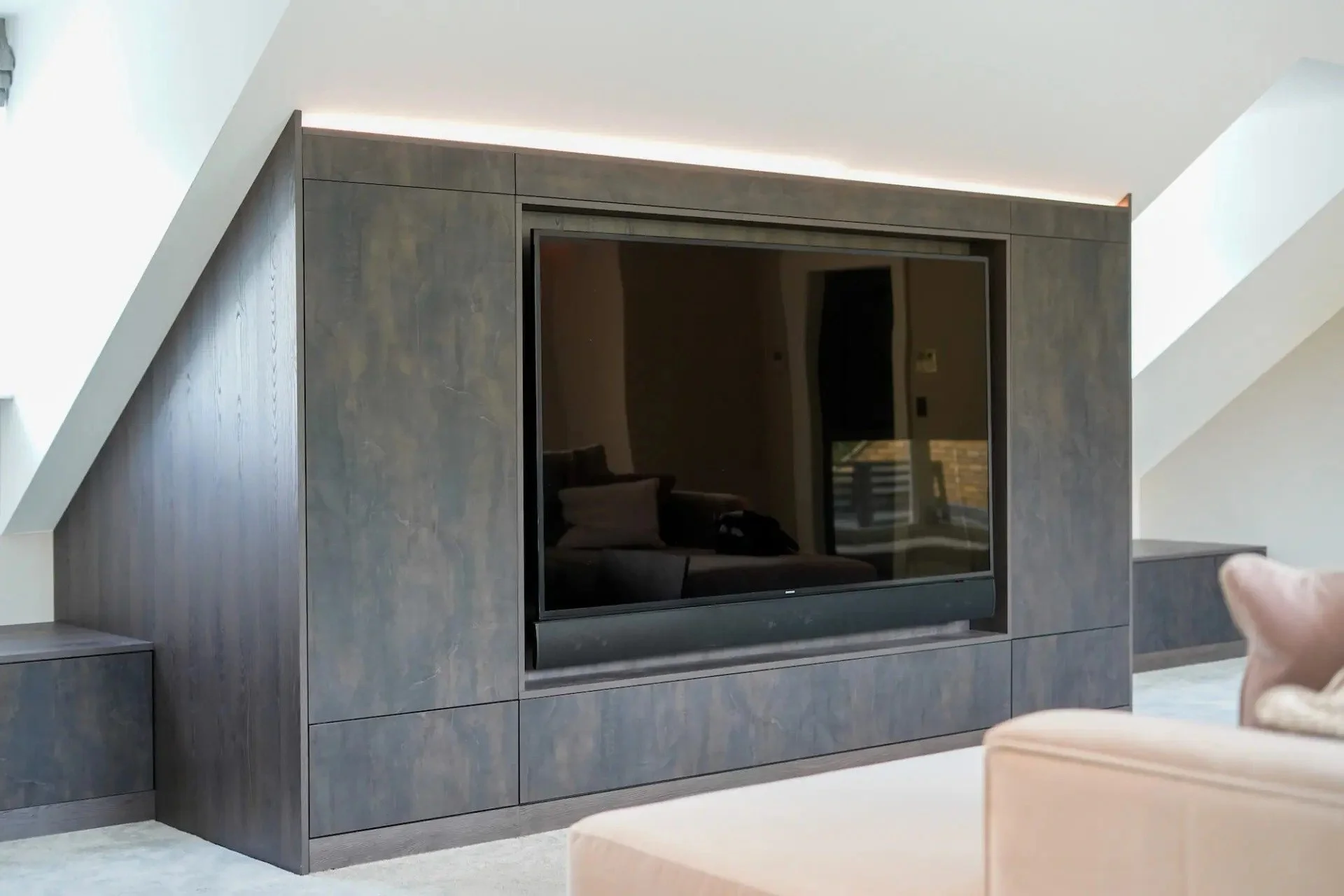A black flat-screen TV mounted inside a wooden cabinet with a matte finish in a modern living room. Part of a beige sofa is visible in the foreground.