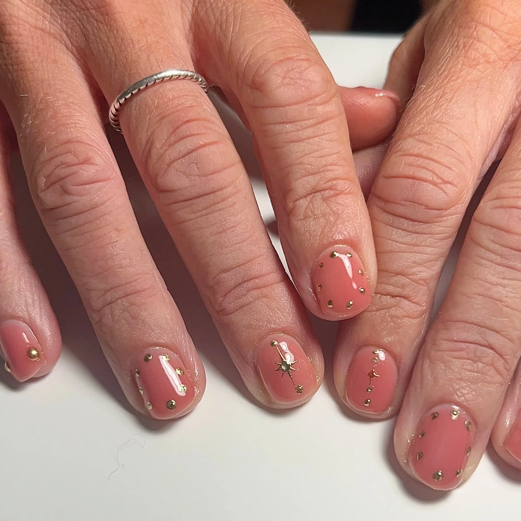 Pink jelly gel manicure with gold chrome stars and dots.