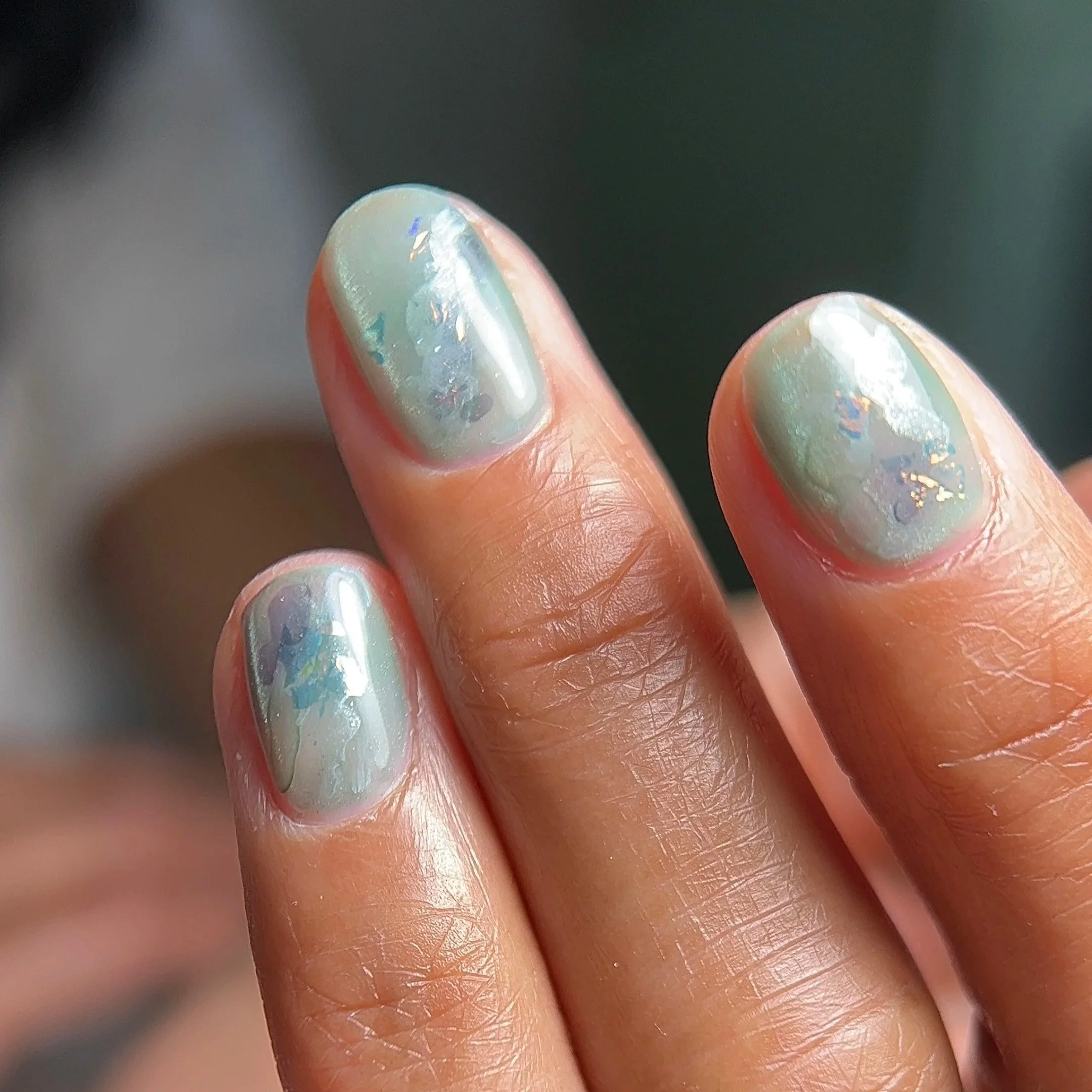 Close-up of fingers with iridescent, multicolored nails that have a swirling pattern.