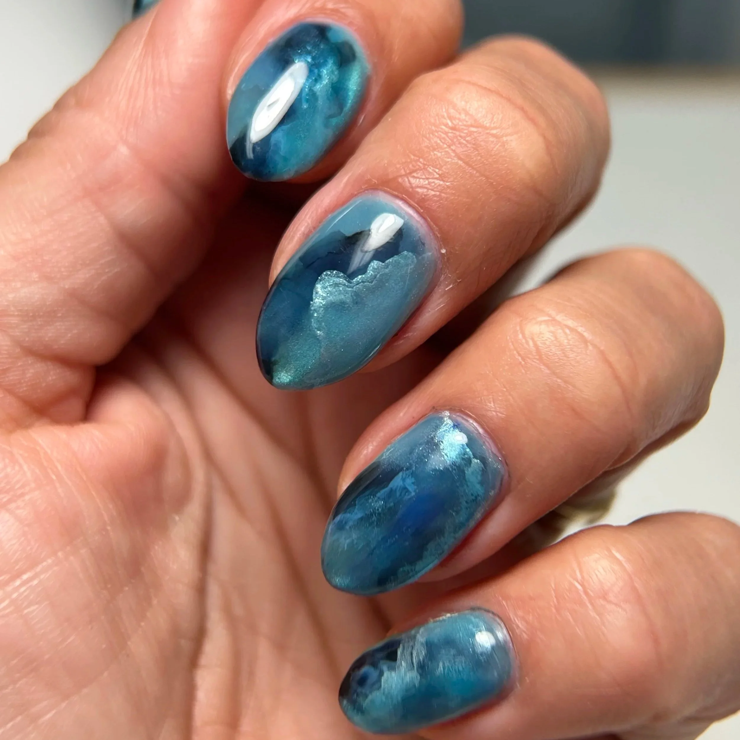 Detailed Japanese and Korean Jel manicured hand with blue, silver, and black swirls.