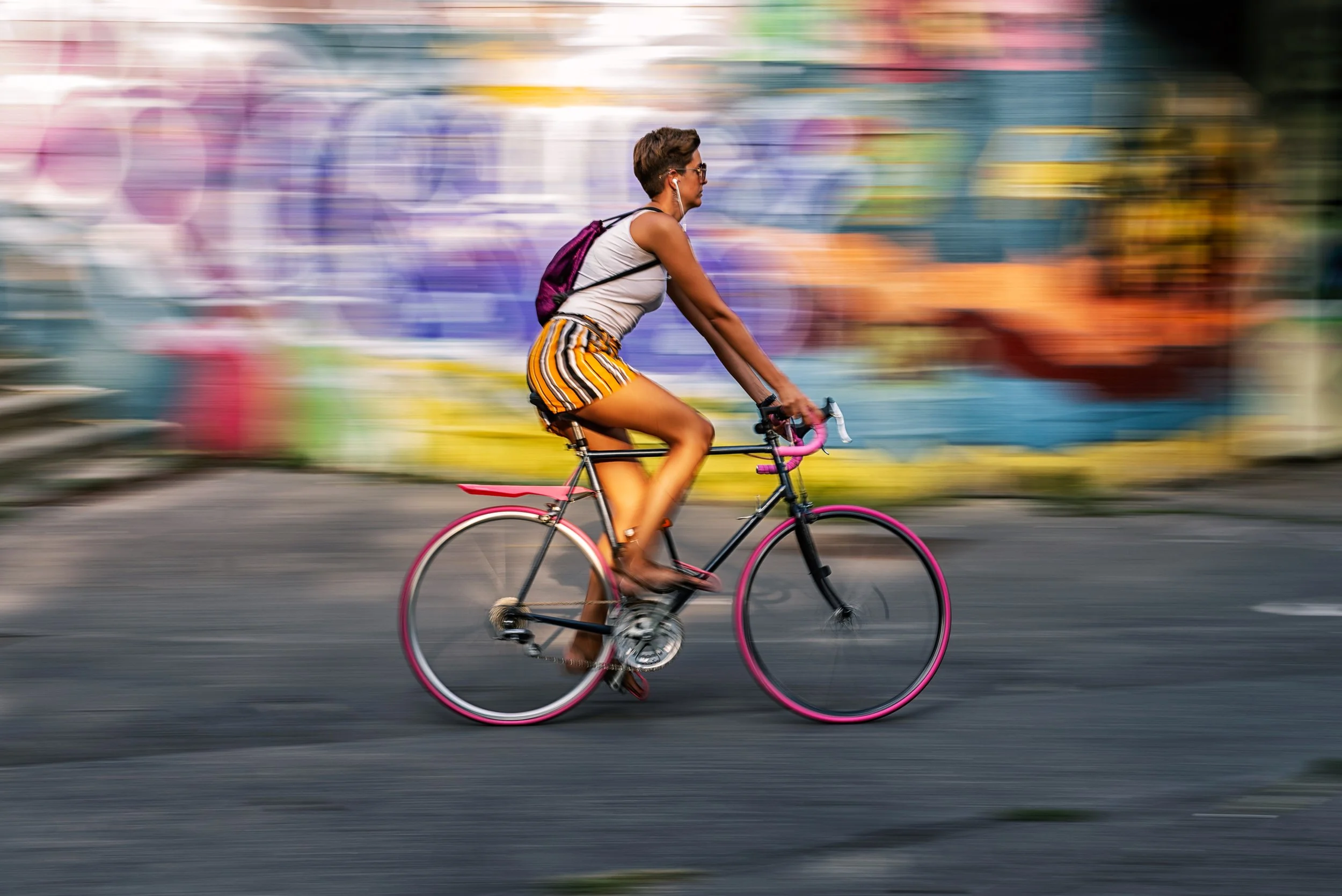 A woman riding a bicycle in front of a colorful graffiti wall with motion blur.