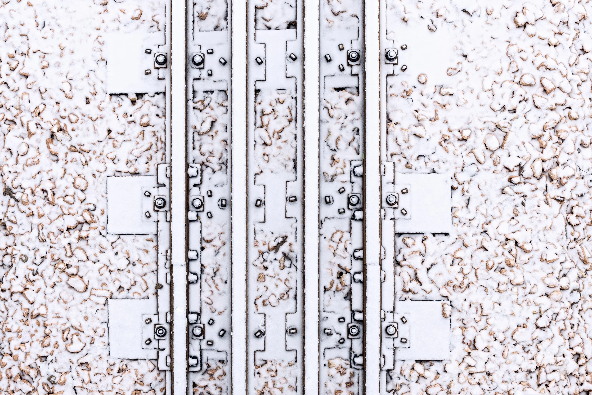 Close-up of train tracks with snow covering the metal rails, surrounded by snow-covered rocks.