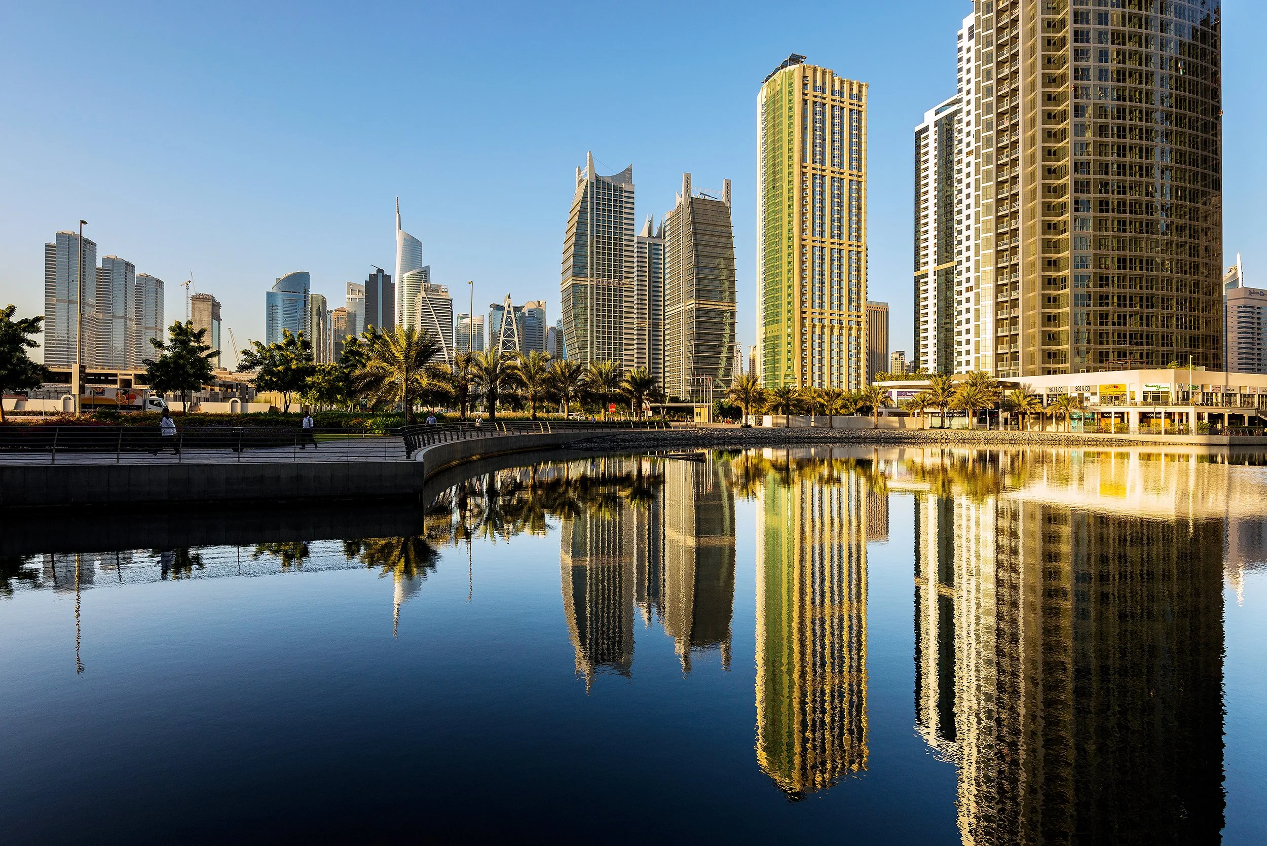 Peter Nemeth photographer. Skyscrapers in a city skyline reflected in a body of water, with a clear blue sky overhead.