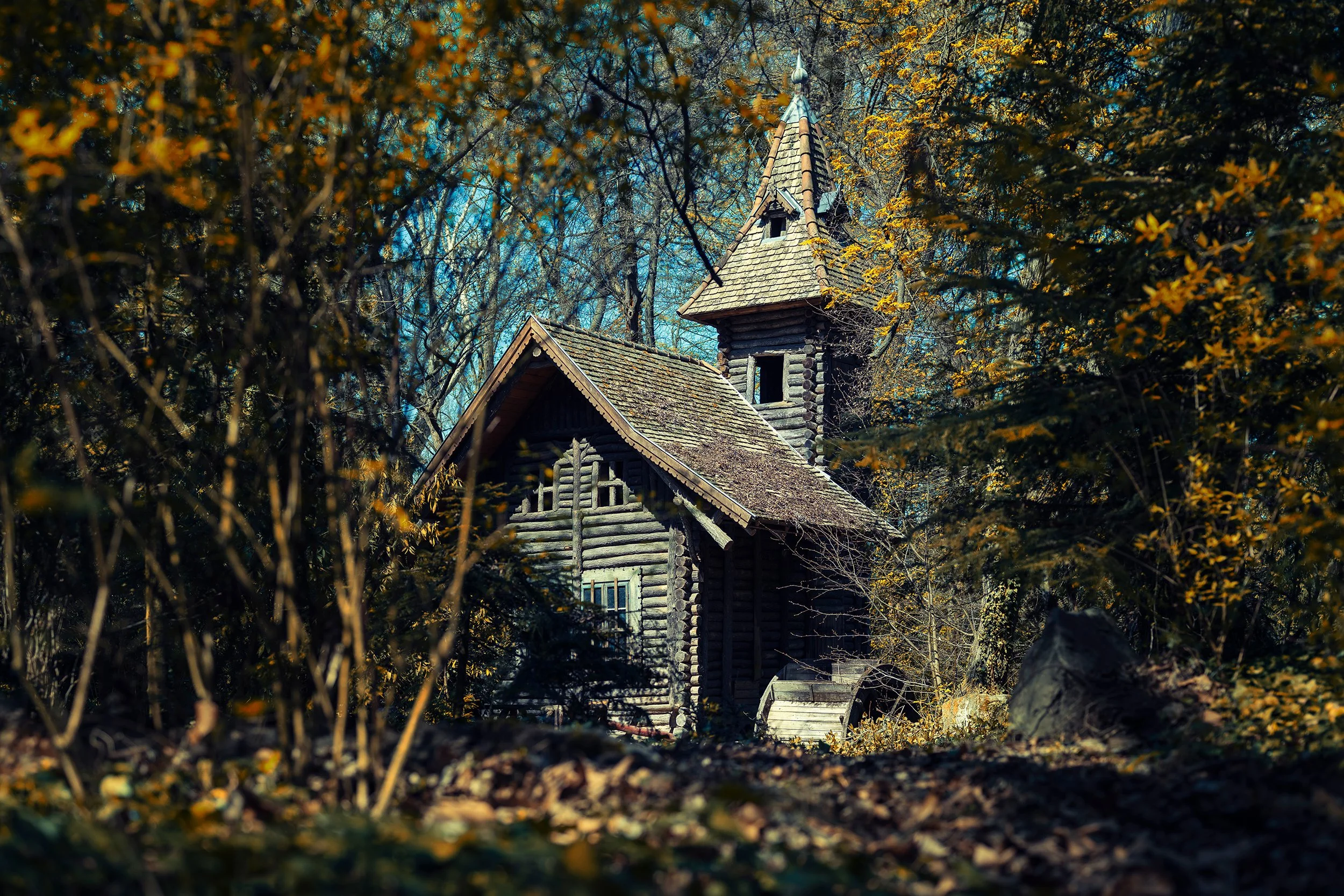 Peter Nemeth photographer. A wooden church building with a steep roof and a small steeple, surrounded by dense trees with autumn leaves.