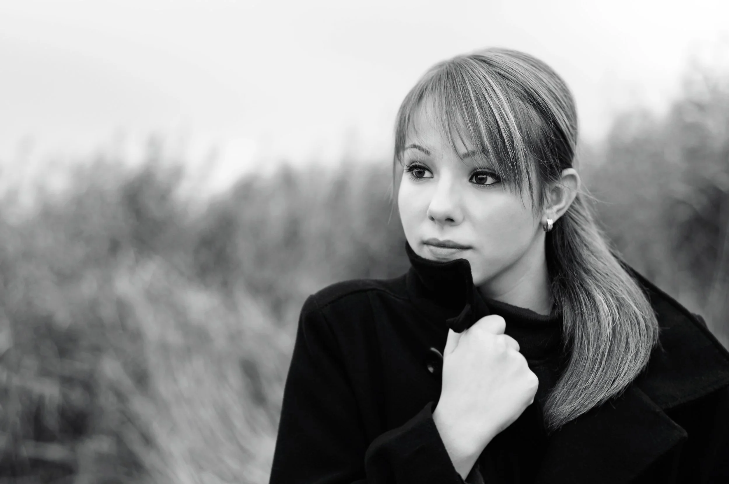 A black and white photo of a young woman with short hair looking to the side, outdoors in a natural setting with blurred trees and grass in the background.