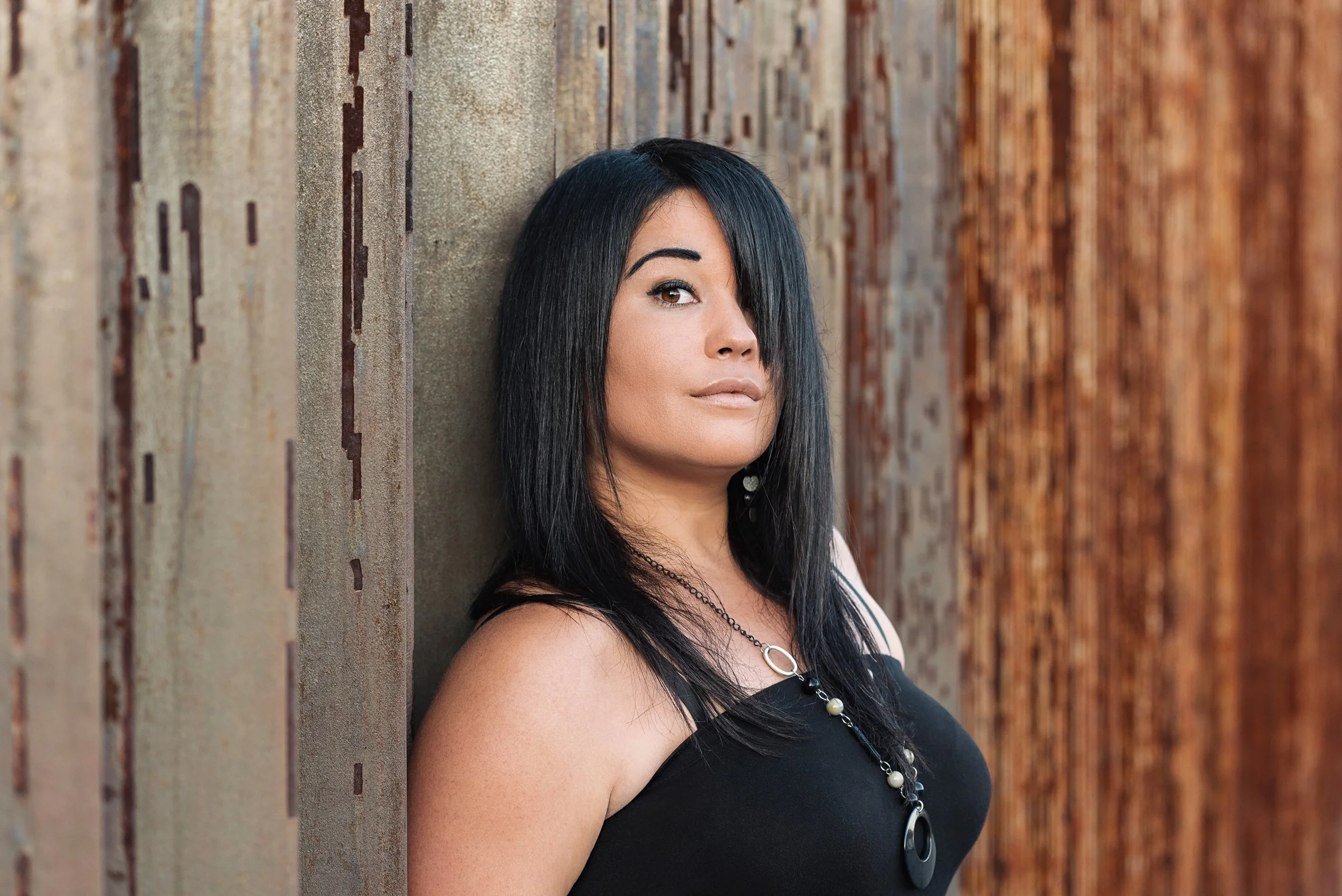 A woman with black hair and light skin posing against a textured wall.
