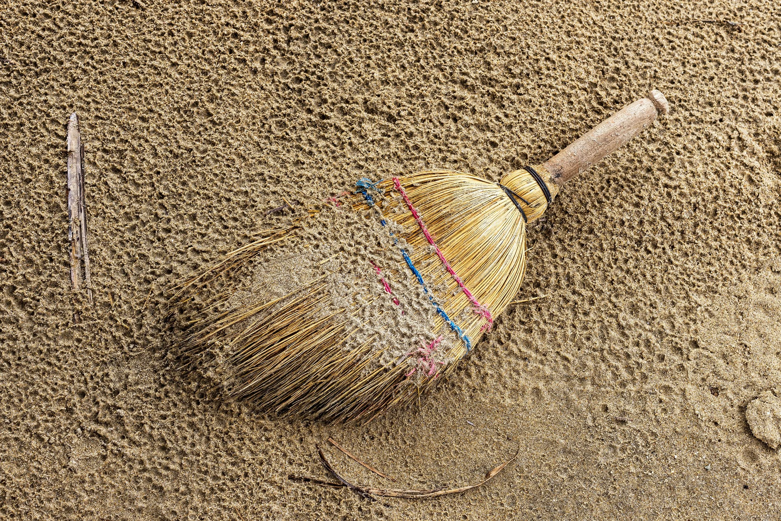 A sandy beach with a straw hat decorated with colorful strings lying on the sand, with a piece of driftwood nearby.