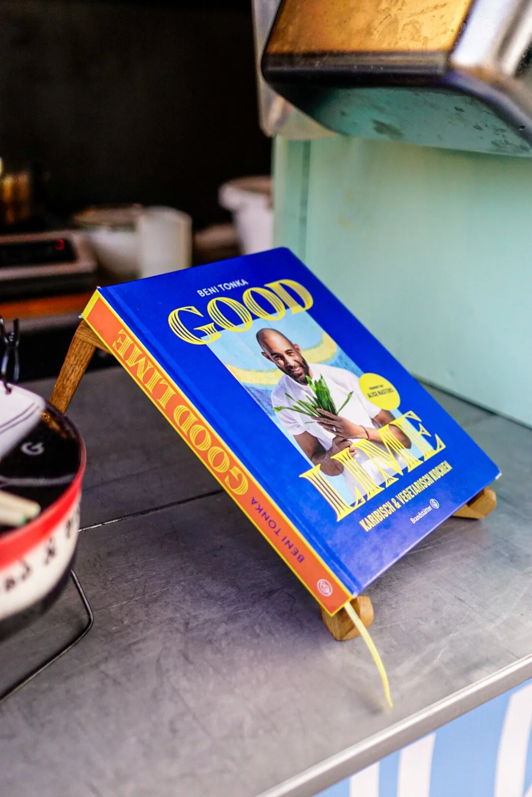 A book titled 'Good Lime' by Beni Tonka displayed on a small wooden stand on a metal countertop.