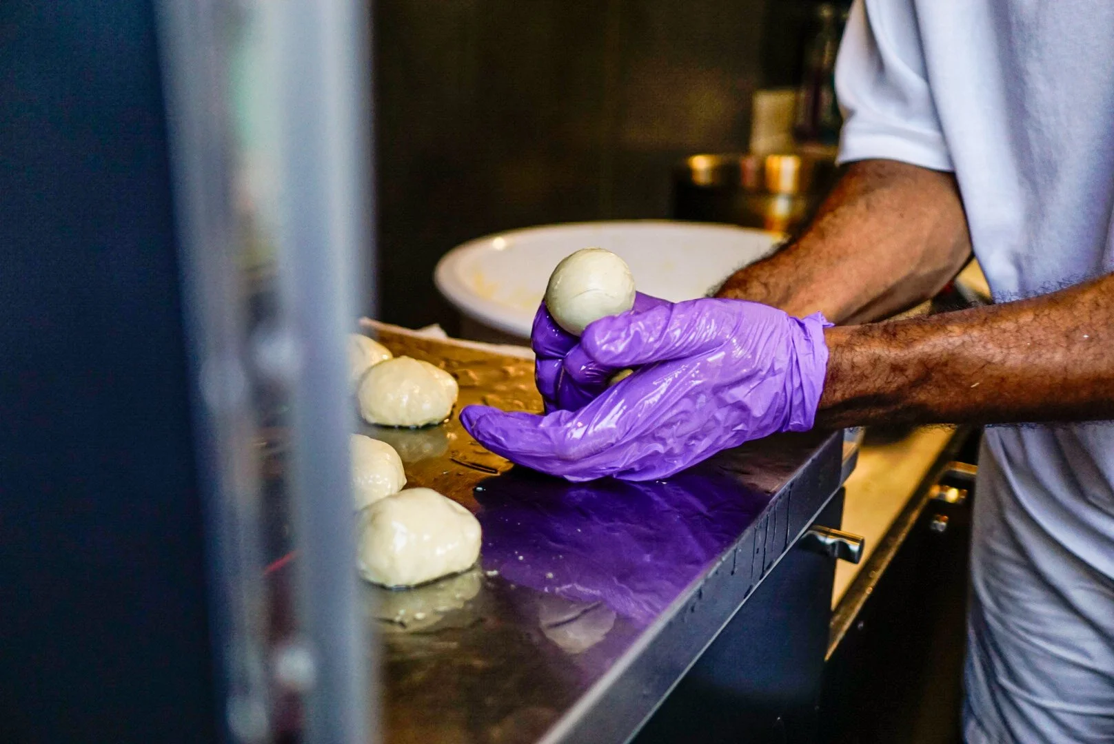 Beni Tonka is wearing purple gloves shaping dough into a ball on a stainless steel counter in his foodtruck.
