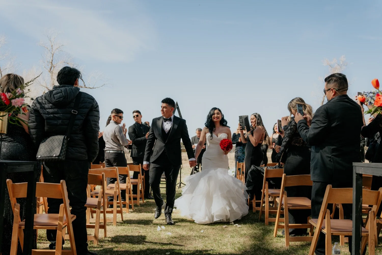 Bride and groom walking up the aisle past cheering guests at an outdoor wedding ceremony