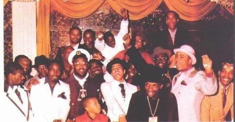 Group of people at a festive event, some wearing costumes and hats, posing for a group photo with decorations in the background.